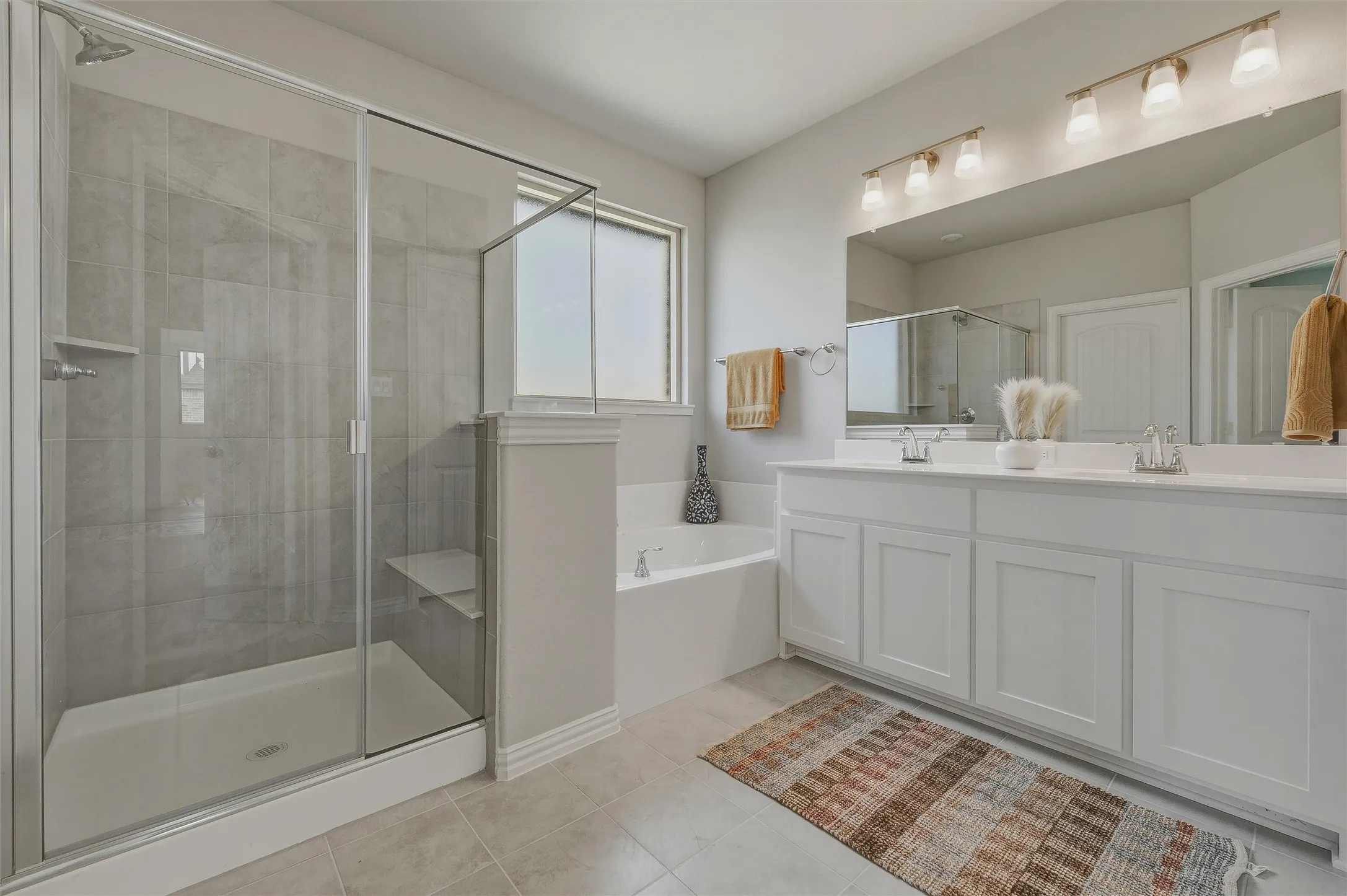 Walk-in shower with glass enclosure, dual vanity with undermount sinks, built-in soaking tub, tile flooring, and overhead vanity lighting