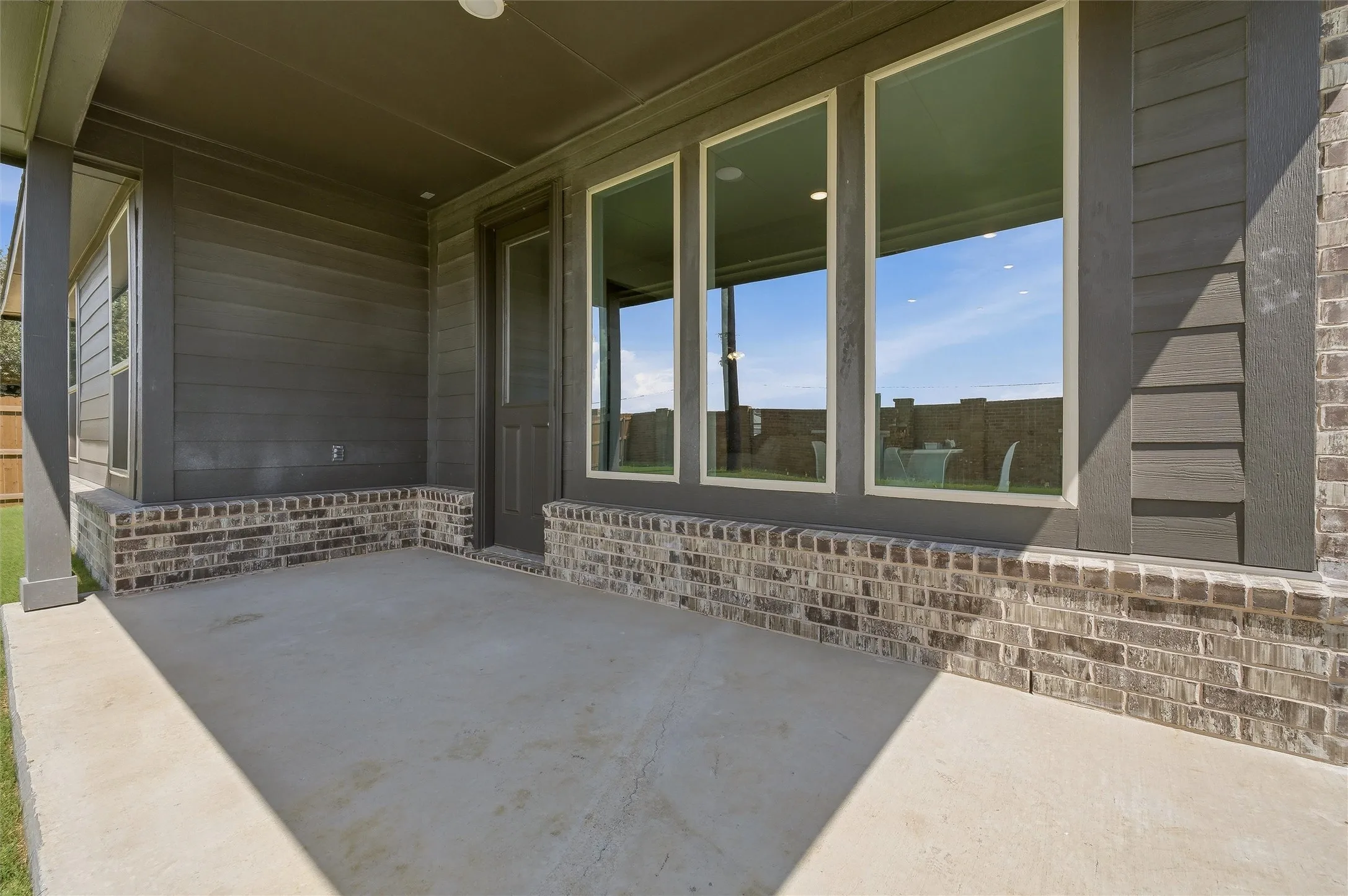 Covered concrete patio featuring a brick foundation and durable siding