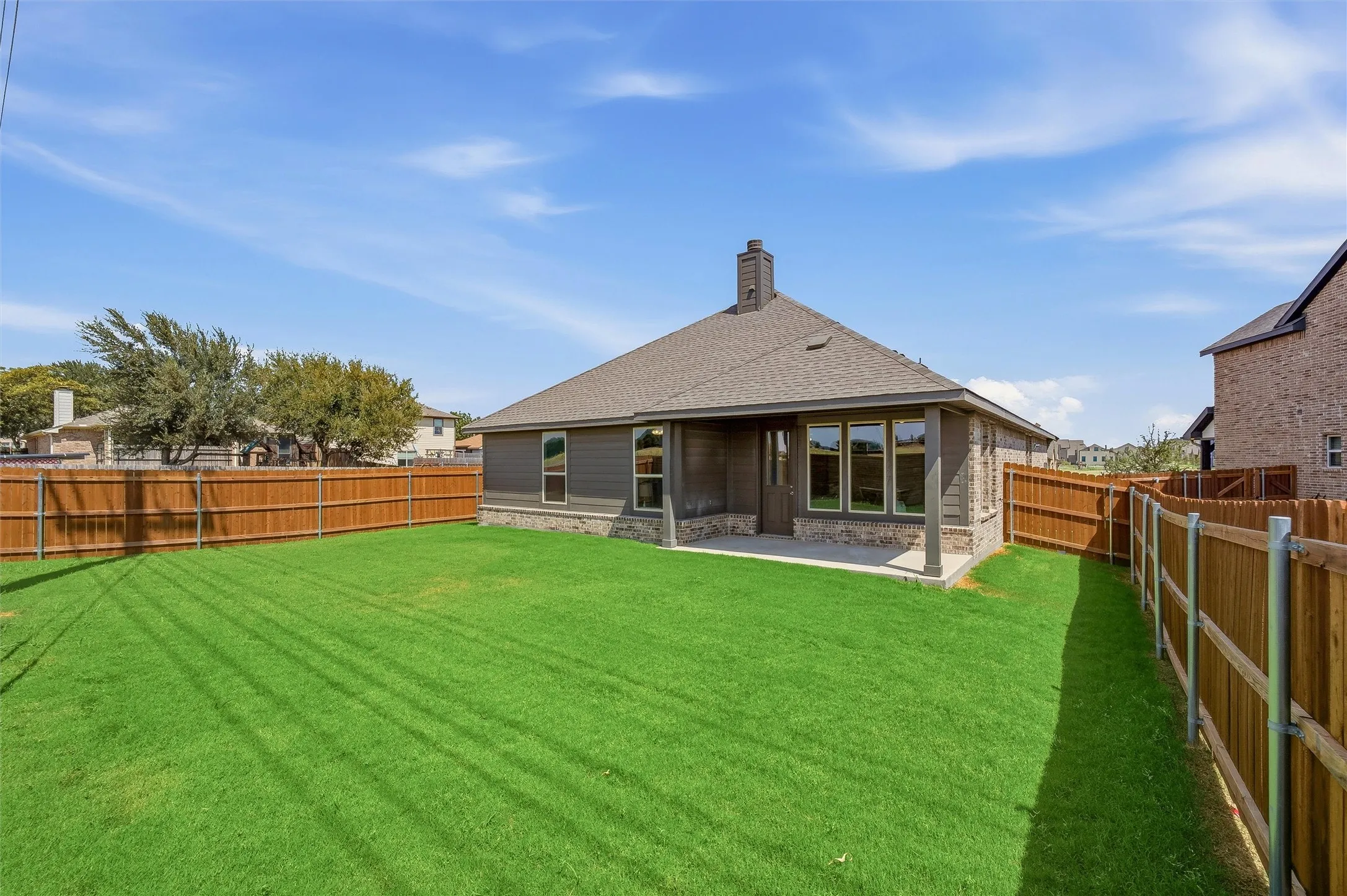 Expansive green lawn, wood privacy fencing, covered patio, multiple windows, and a brick and siding exterior
