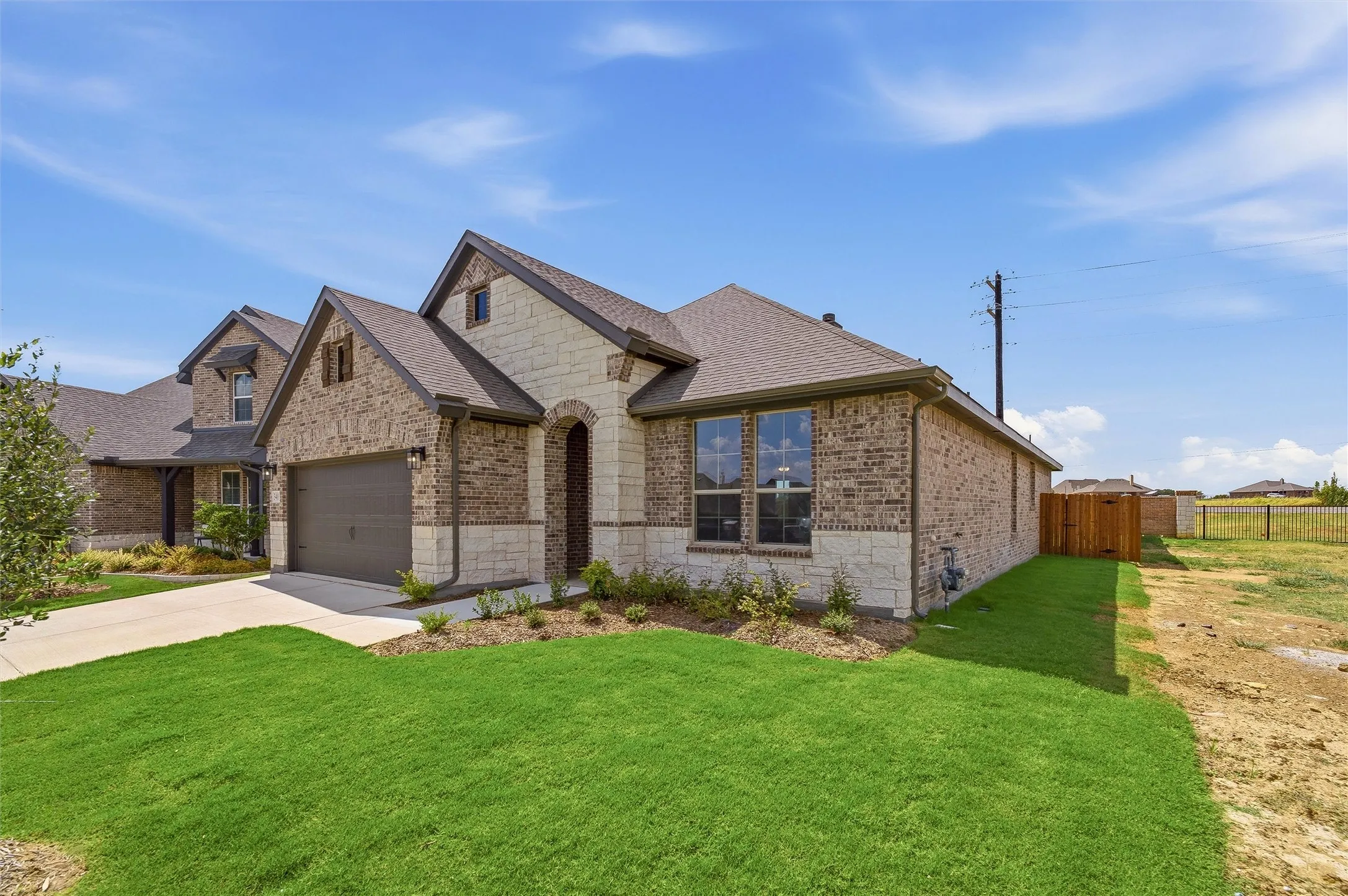 Single-story residence featuring a brick and stone exterior, an arched entryway, an attached two-car garage, and a brown shingle roof