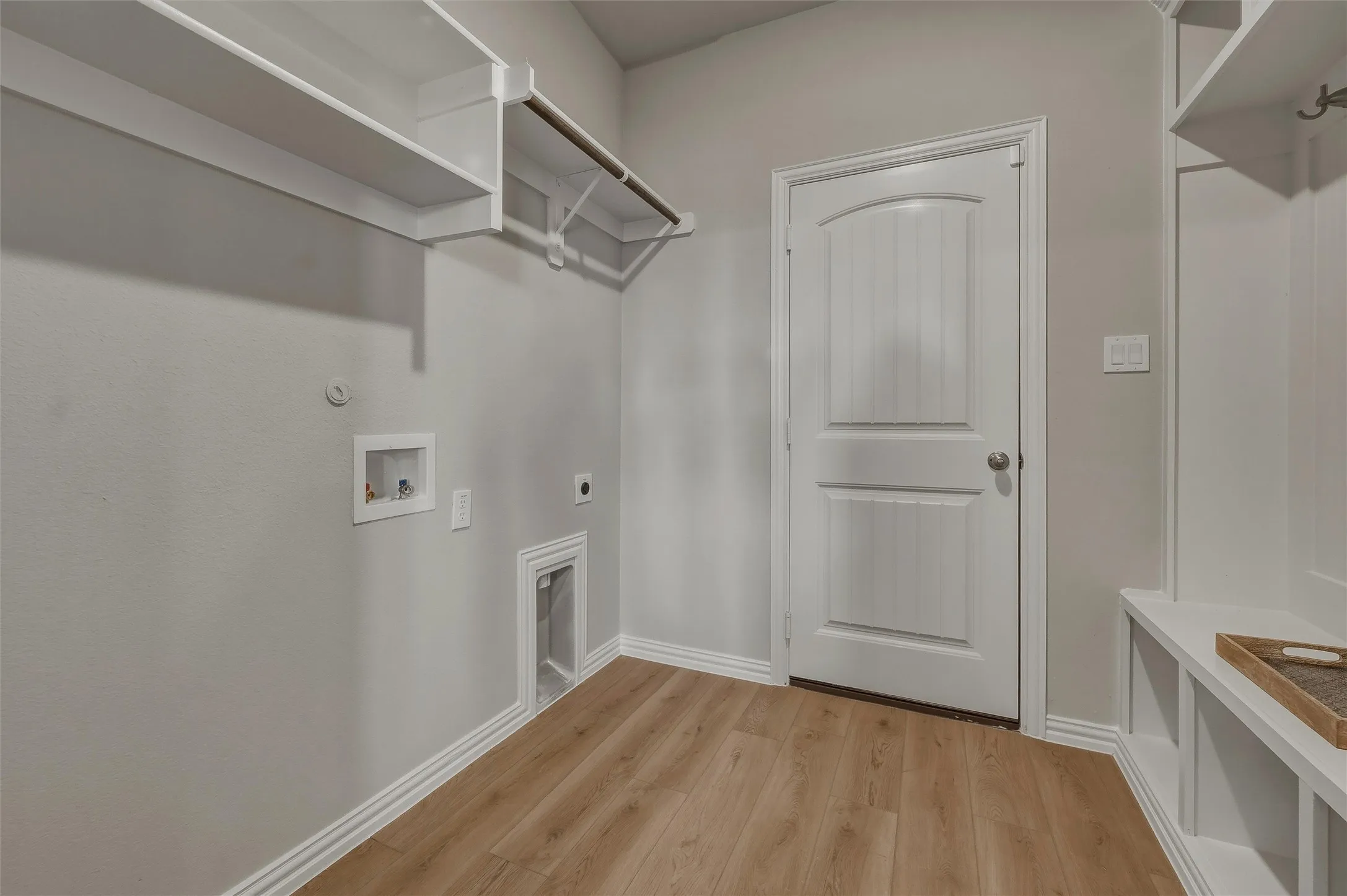 Laundry area with wood-finish flooring, built-in shelving, hanging rod, and wall-mounted hooks