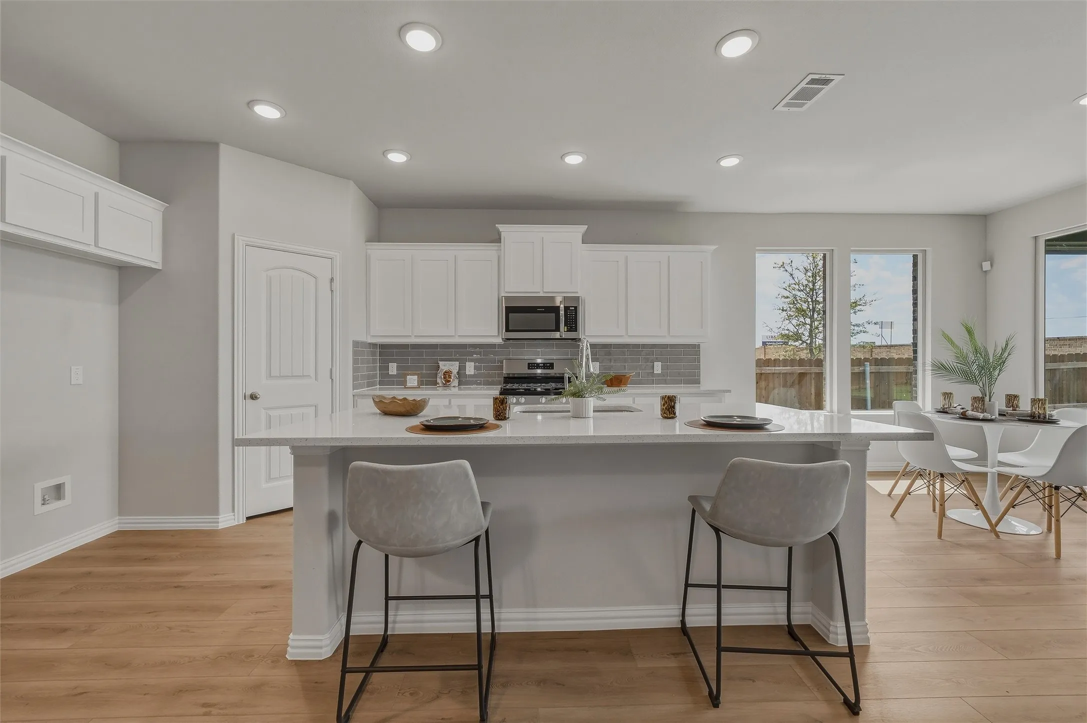 Recessed lighting, wood-finish flooring, white cabinetry, integrated stainless steel microwave, and large windows