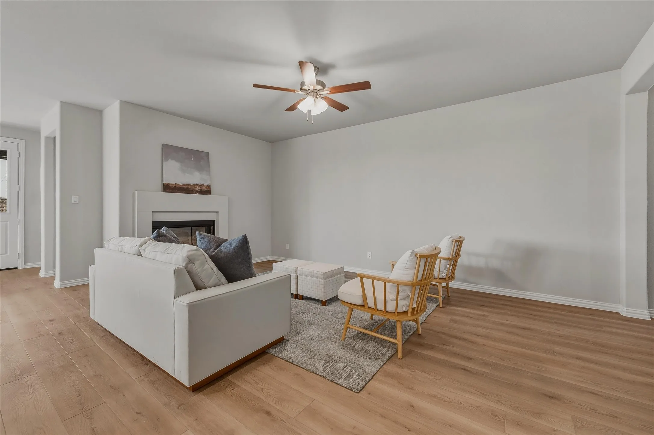 Living space featuring wood-finish flooring, a fireplace with a mantel, a ceiling fan with integrated lighting, and light-toned walls
