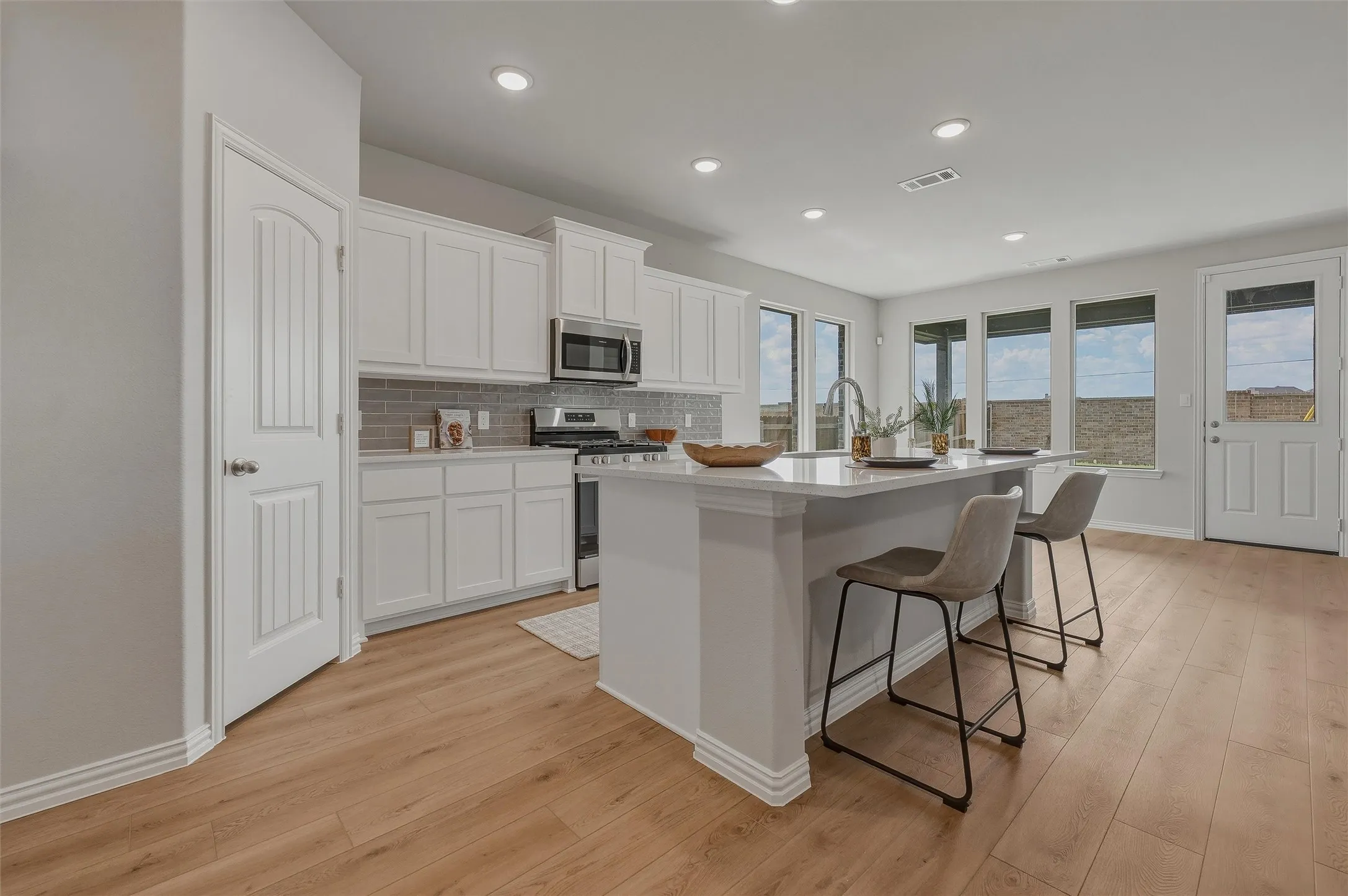 Modern kitchen featuring white cabinetry, a large island with seating, stainless steel appliances, and wood-finish flooring