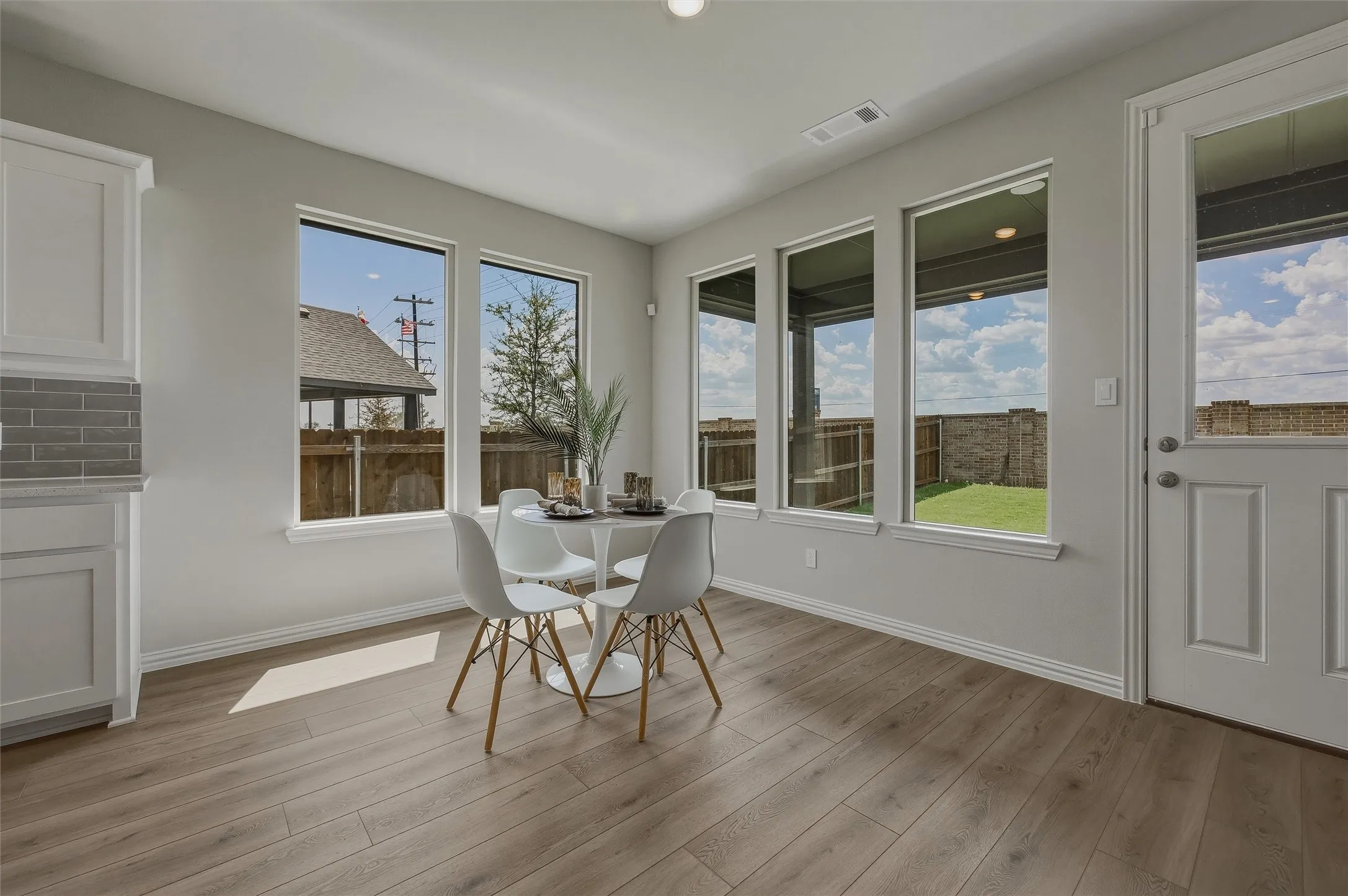 Wood-finish flooring, white cabinetry, gray subway tile backsplash, and multiple windows