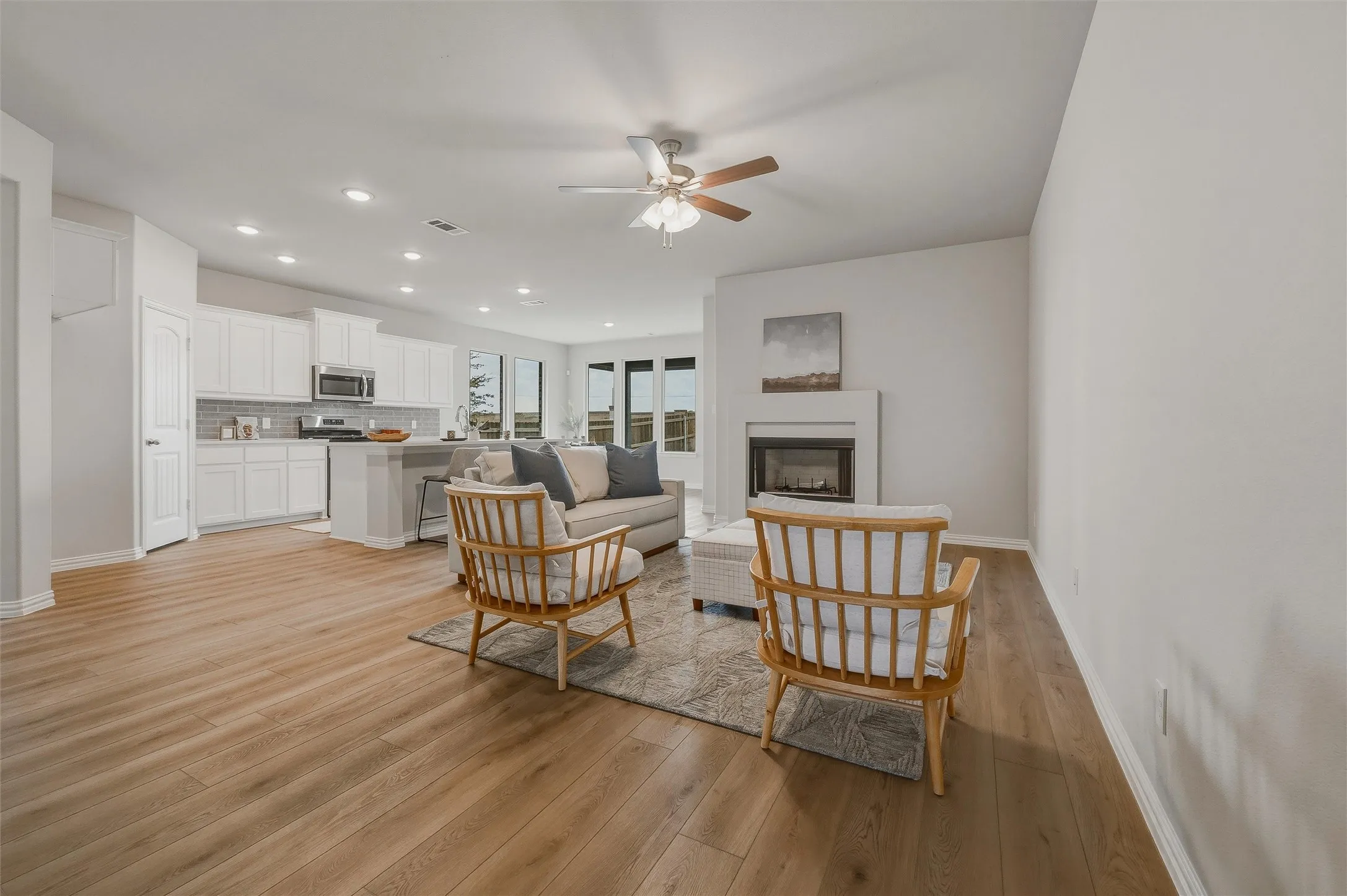 Open-concept living area with wood-finish flooring, a contemporary fireplace, and a ceiling fan