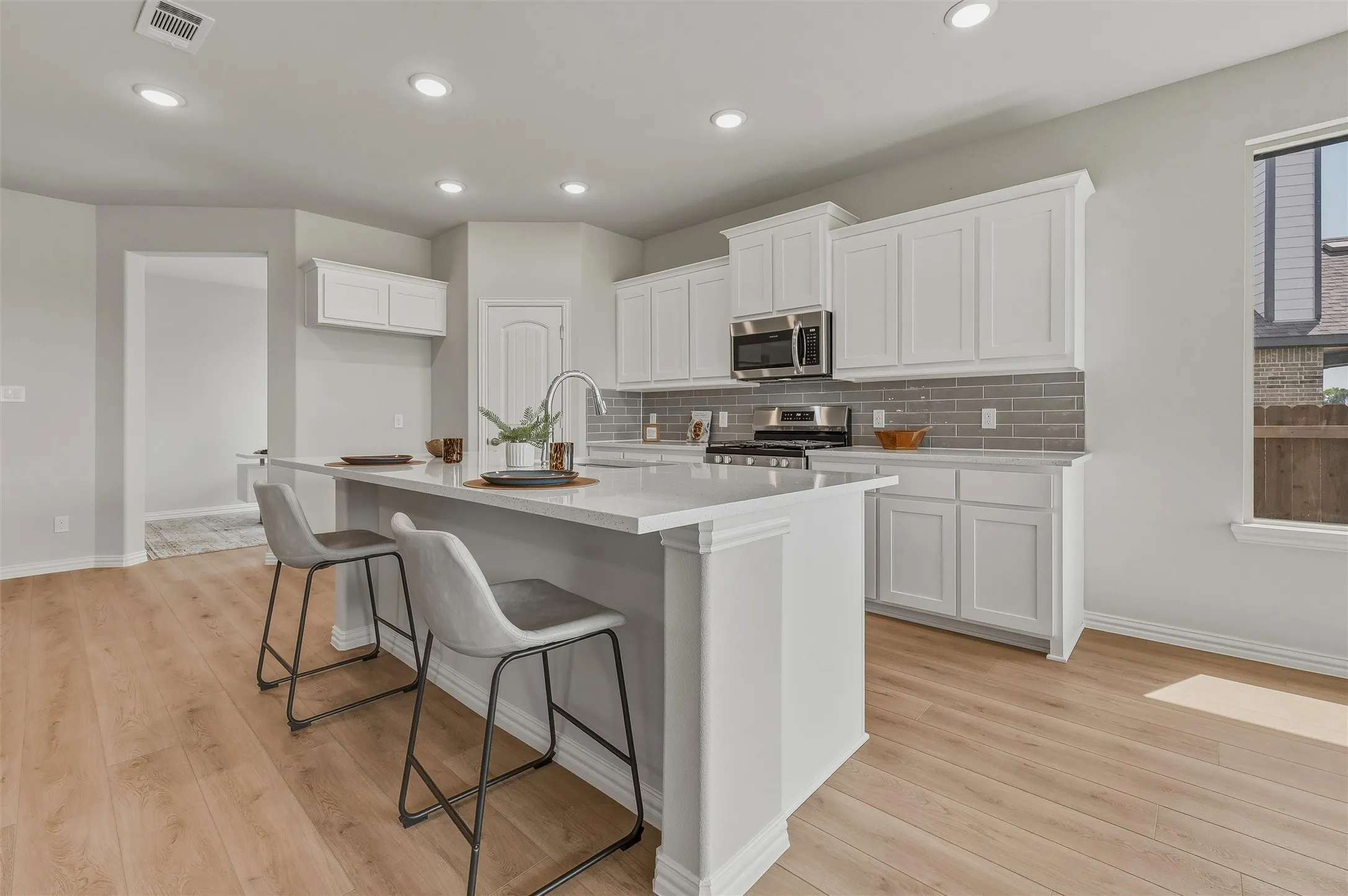 Kitchen featuring white cabinetry, light-colored countertops, stainless steel appliances, a gray subway tile backsplash, and wood-finish flooring