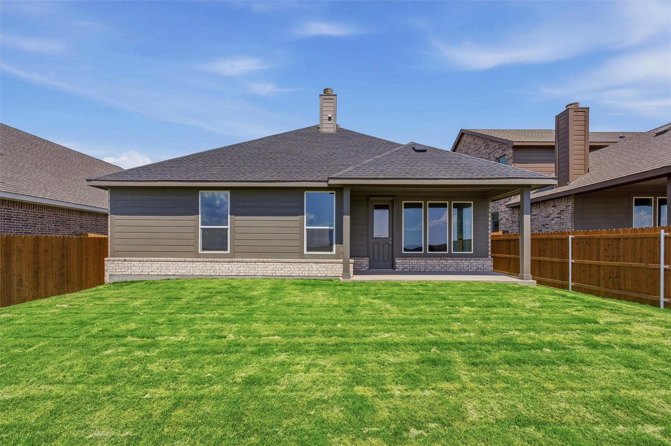 Expansive backyard featuring a manicured lawn, full privacy fencing, covered patio, and a shingle roof