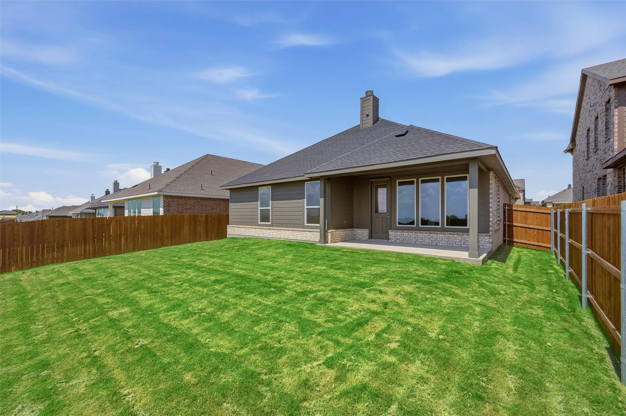 Expansive grassy backyard featuring a covered patio, wood fencing, and multiple large windows