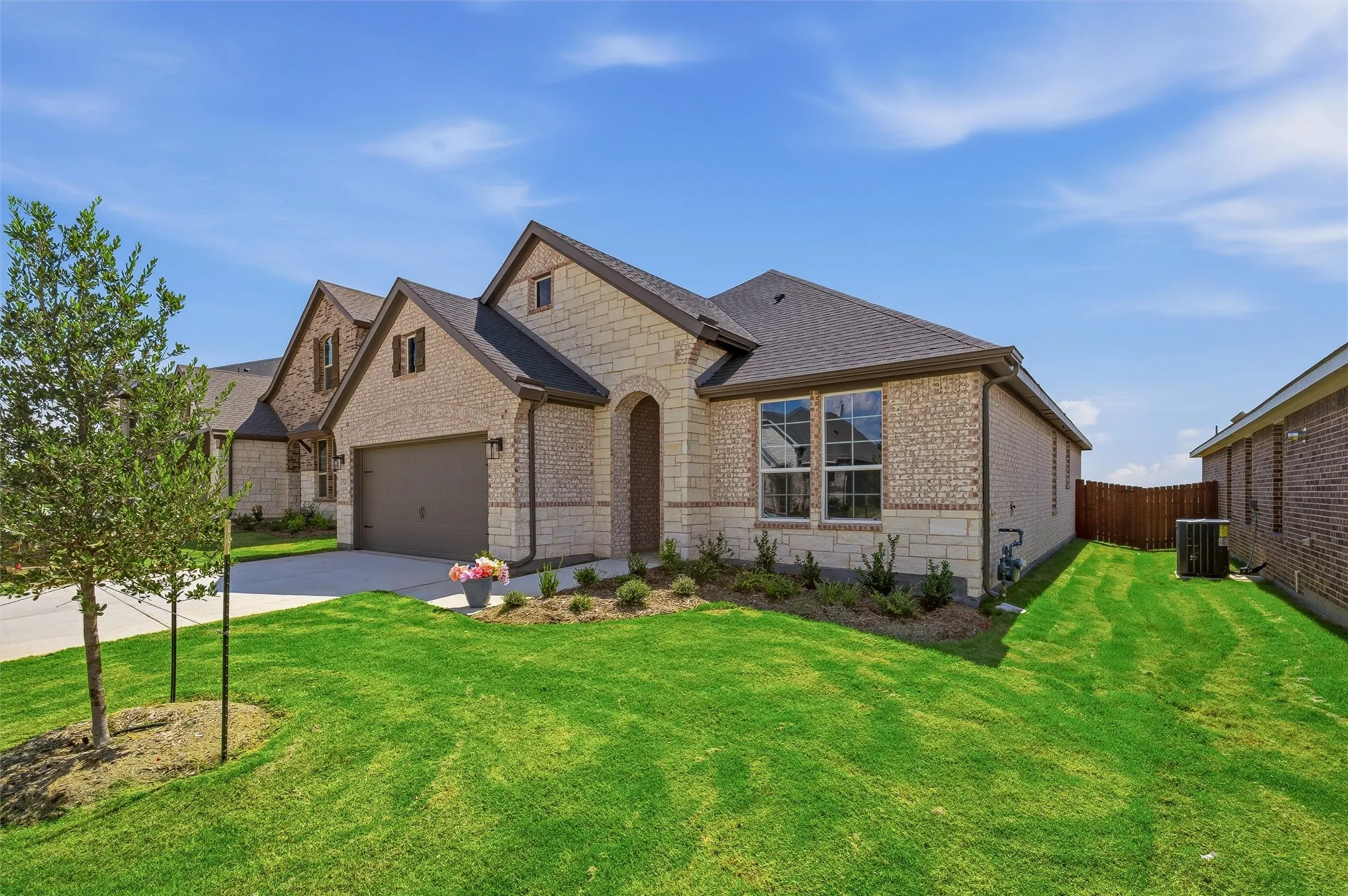 Brick and stone facade, arched entryway, attached garage, gabled rooflines, and a planted landscape