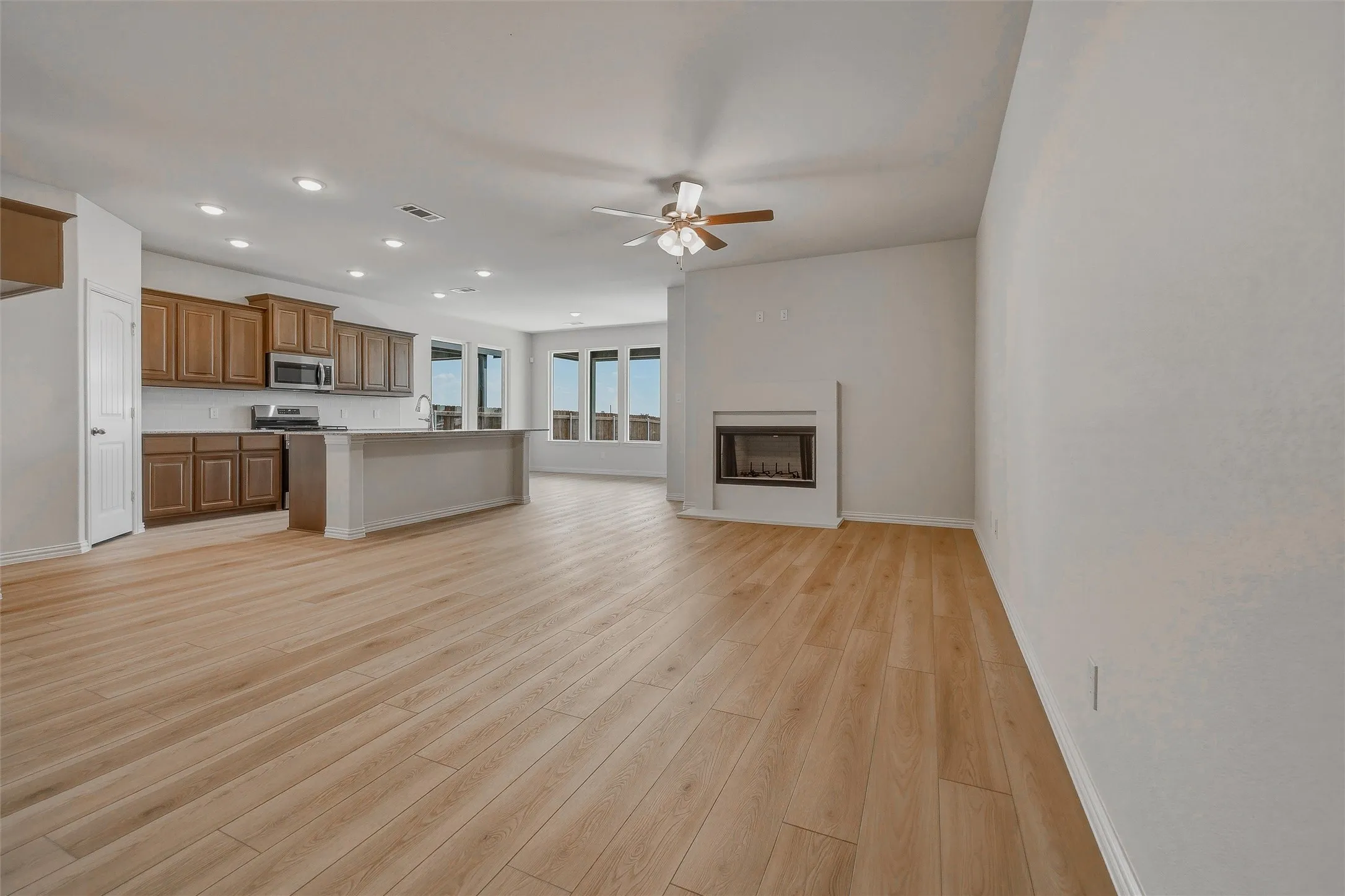 Wood-finish flooring throughout, kitchen with wood cabinetry and stainless steel appliances, central island, multiple windows, and a built-in fireplace