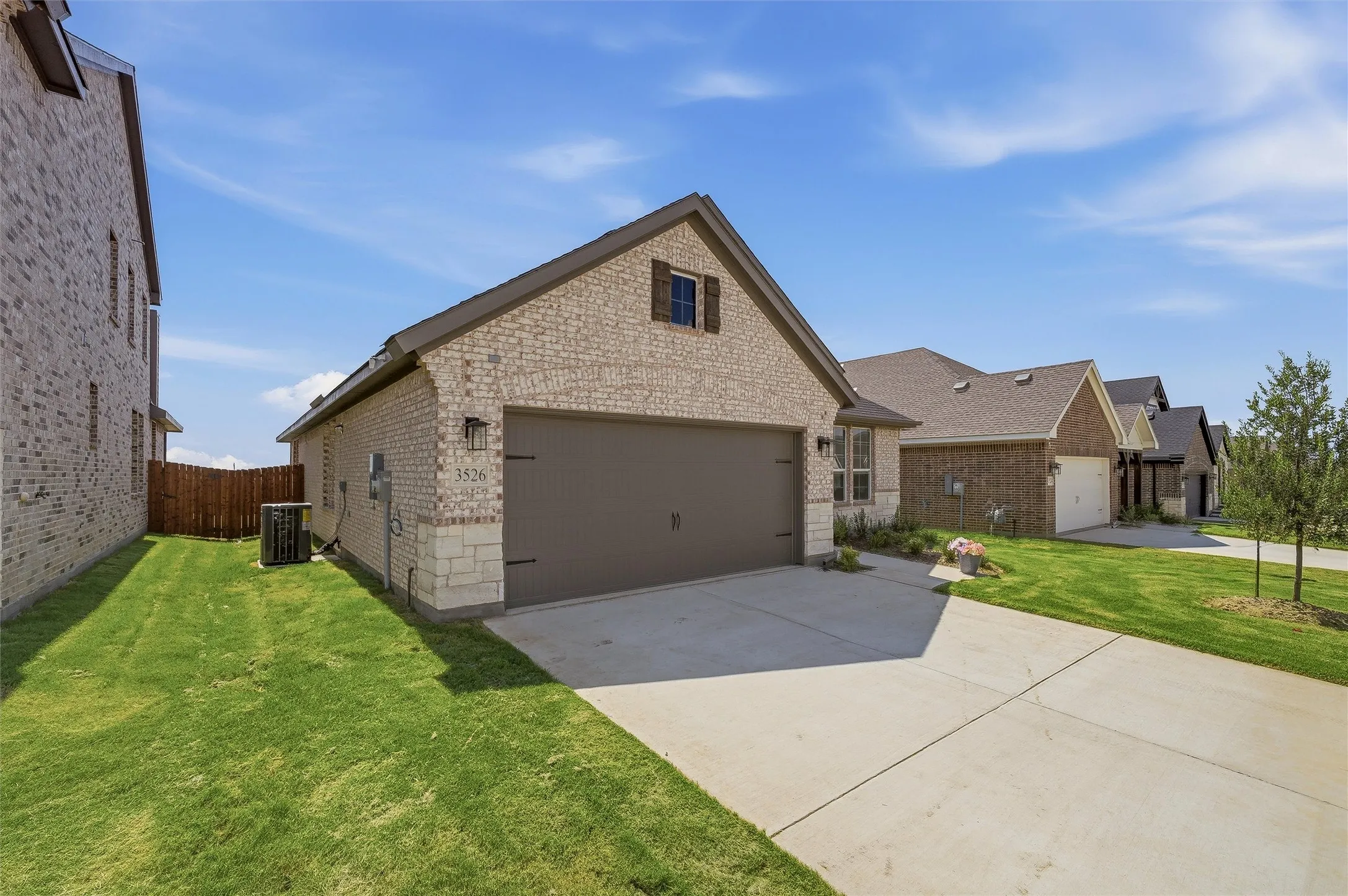 Brick exterior with stone accents, attached garage with carriage-style door, concrete driveway, and established front lawn