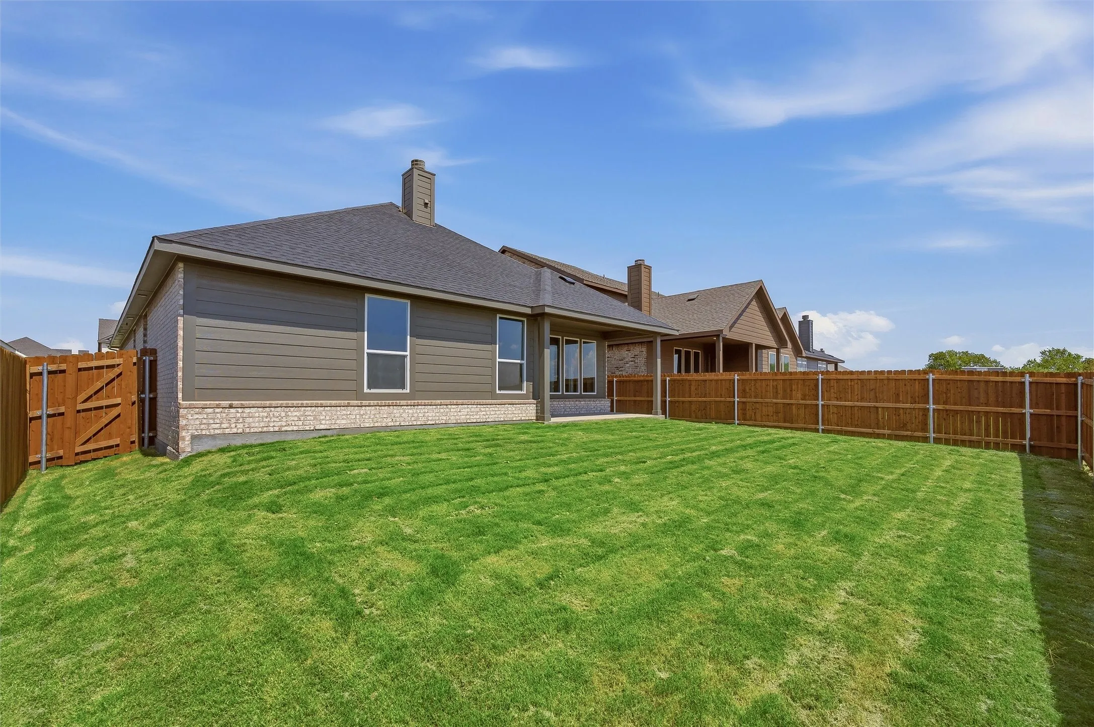 Expansive rear yard with a manicured lawn, full privacy fencing, and a wood gate