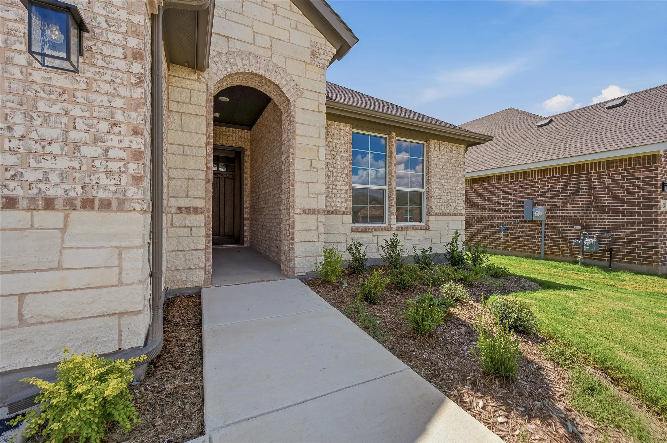 Brick and stone facade, arched entryway, dark-paneled door, double-paned windows, and a landscaped front yard