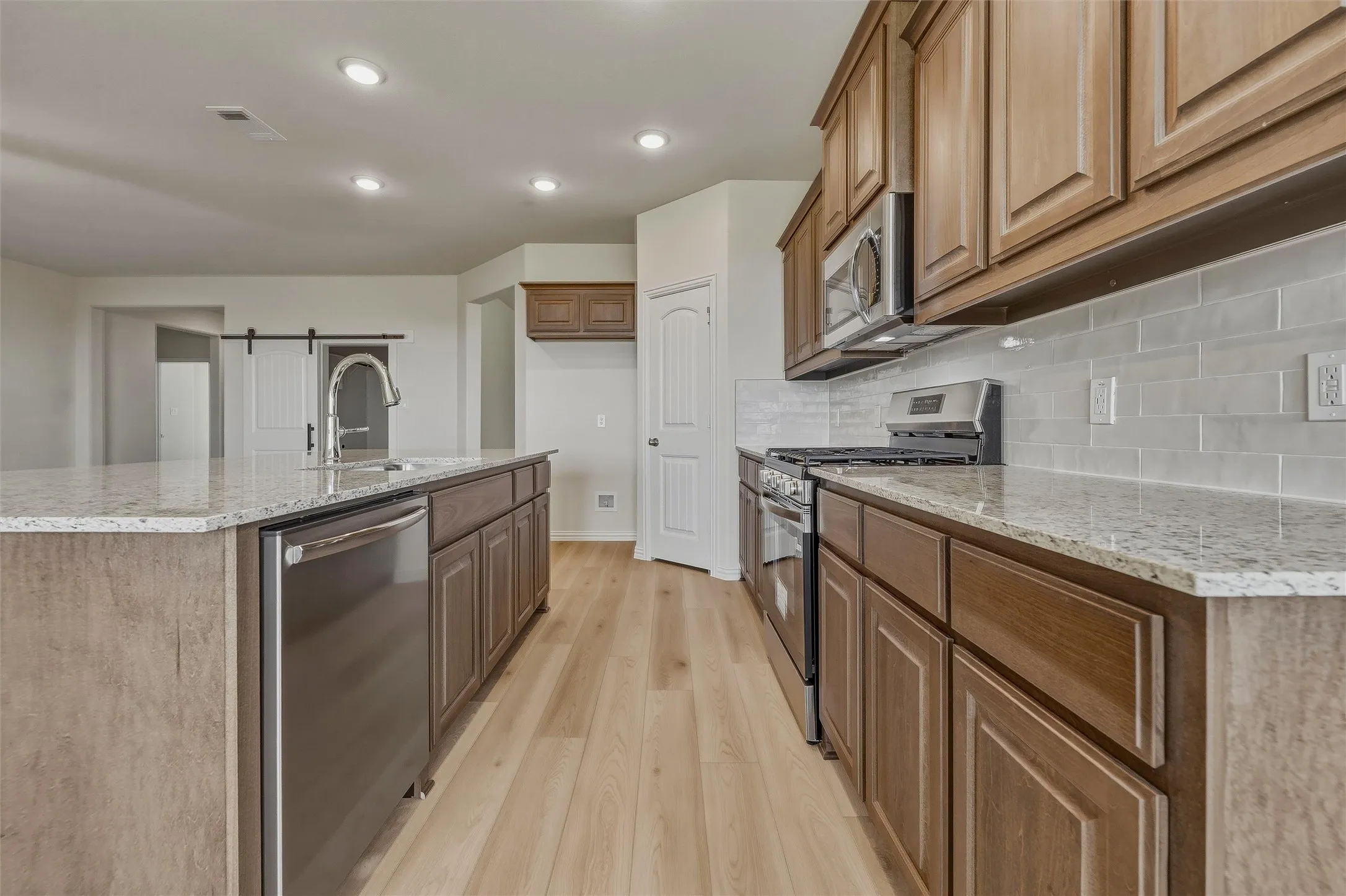 Kitchen featuring wood-finish flooring, recessed lighting, a kitchen island with an integrated sink and dishwasher, wood cabinetry, and stainless steel appliances