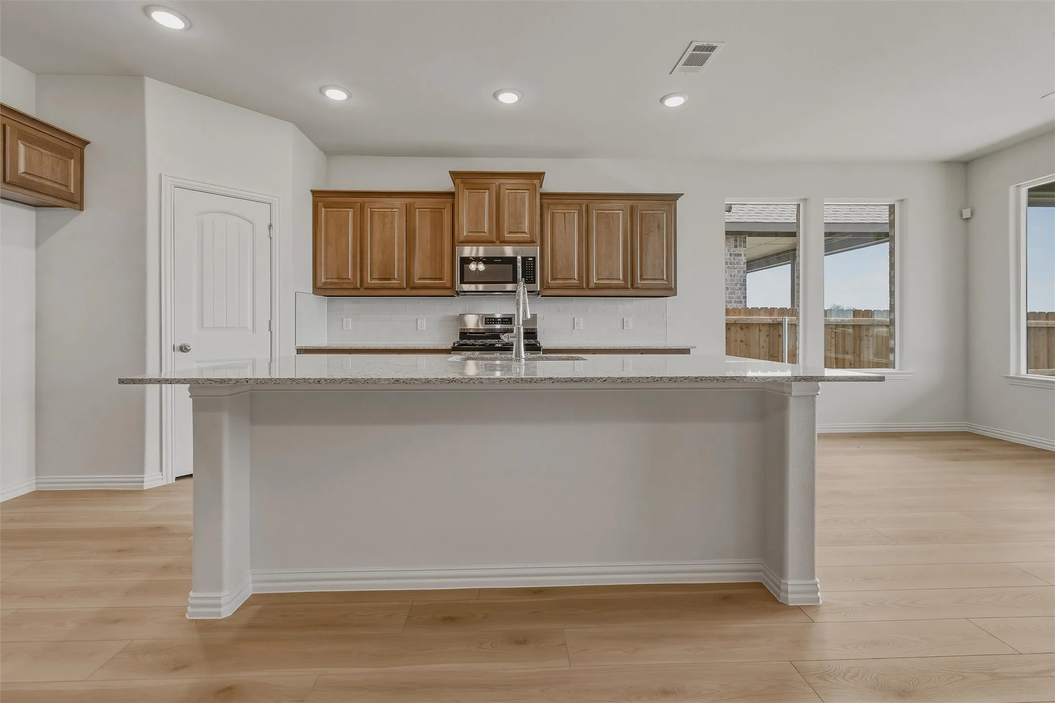 Kitchen island with a granite countertop, recessed lighting, wood-finish flooring, and wood cabinetry
