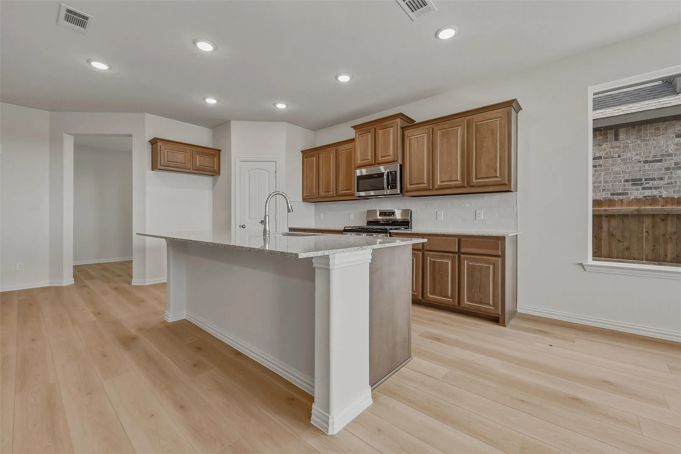 Kitchen featuring wood-finish flooring, recessed lighting, a central island with an integrated sink, shaker-style cabinetry, and stainless steel appliances