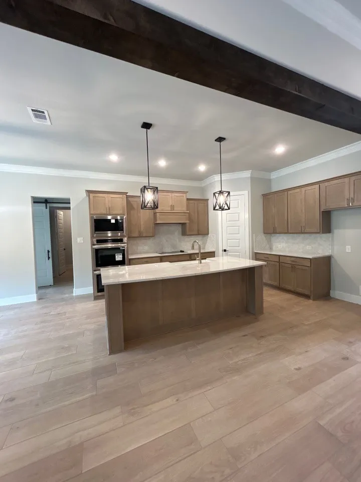 Wood-finish flooring, recessed lighting, wood beam ceiling accent, pendant lighting, and a kitchen island with stone countertop