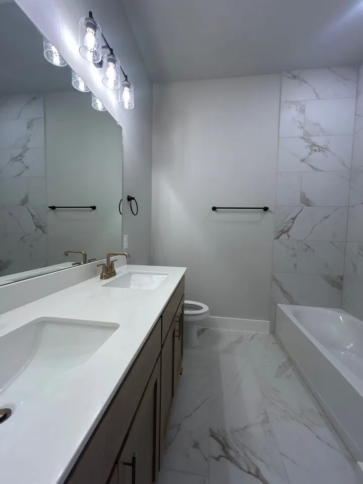 Dual basin vanity with white countertops, matte black vanity pulls, and a multi-light fixture