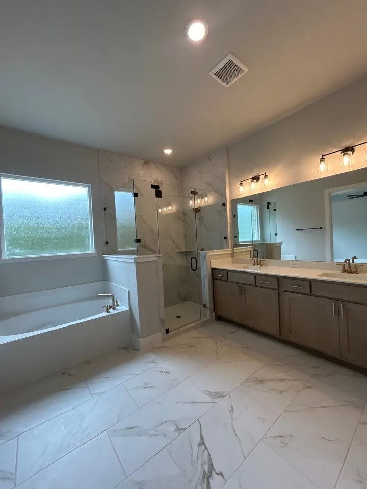 Dual vanity with undermount sinks and light-toned cabinetry, large frameless mirrors, walk-in shower with clear glass enclosure, built-in soaking tub, and tile flooring