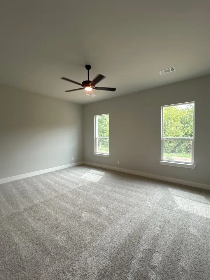 Spacious room featuring plush carpeting, dual windows, and a ceiling fan with integrated lighting
