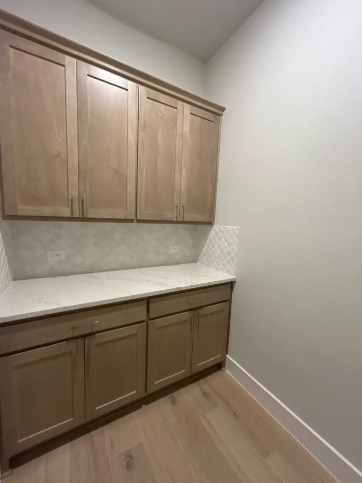 Built-in cabinetry with crown molding, quartz countertops, tile backsplash, and wood-finish flooring