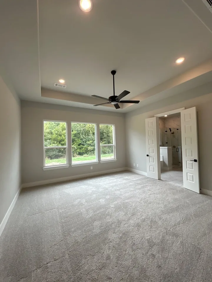 Tray ceiling with recessed lighting, large windows, ceiling fan with black finish, light gray wall paint, and gray carpet