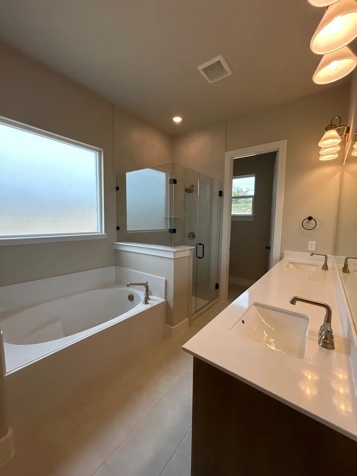 Spacious bathroom featuring a soaking tub, glass-enclosed shower, dual vanity with undermount sinks, and tile flooring