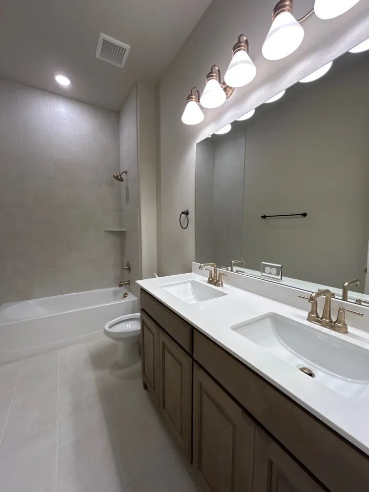 Double vanity with integrated sinks, white countertops, wood-finish cabinetry, and brushed brass fixtures