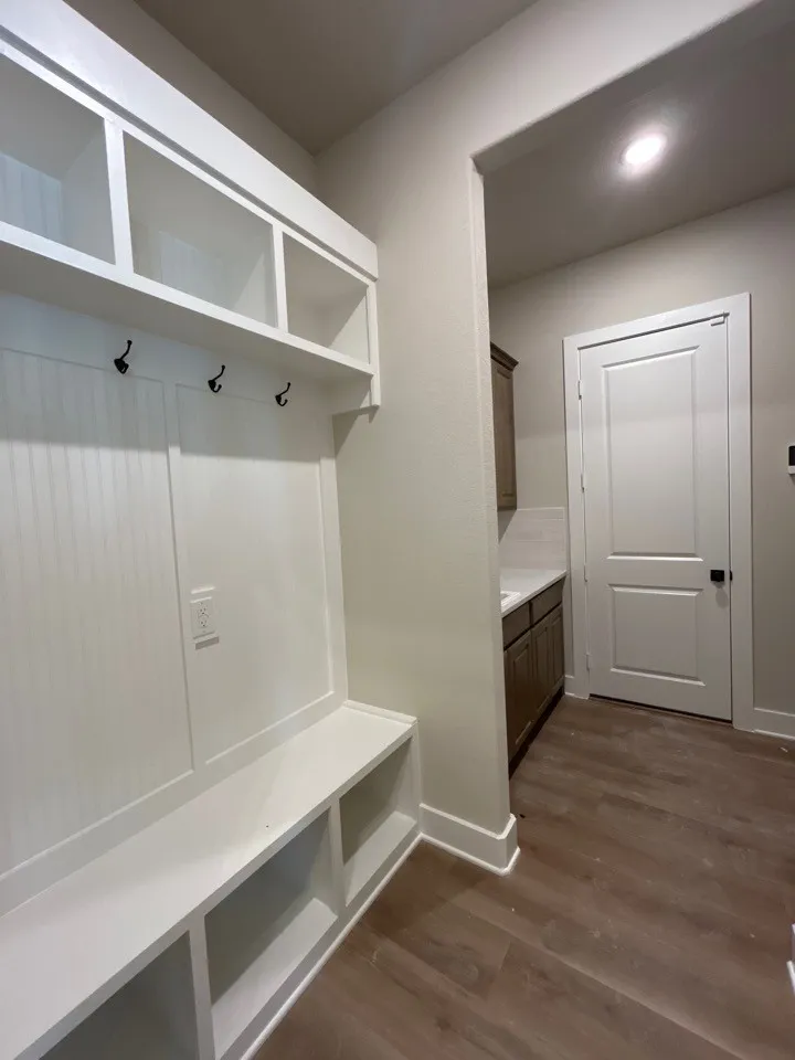 Built-in white mudroom bench with open storage, upper cubbies, and coat hooks