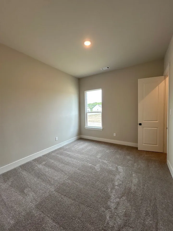 Neutral tone wall paint, recessed ceiling light, white trim baseboards, white paneled door with black hardware, and carpet flooring