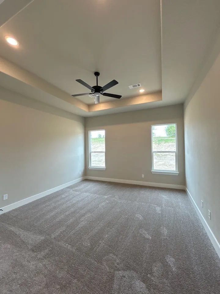 Tray ceiling with recessed lighting, ceiling fan, two windows, wall-to-wall carpeting, and neutral wall tones
