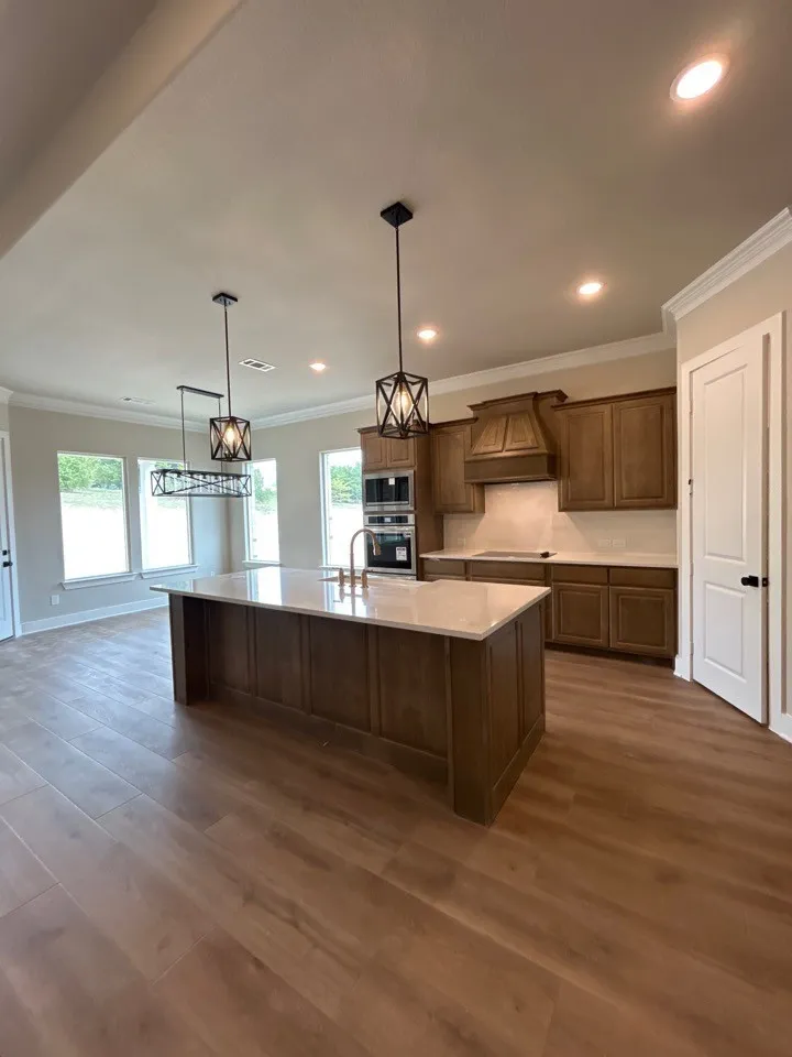 Spacious kitchen featuring a large island with light-toned countertop, wood-finish flooring, recessed lighting, and modern pendant fixtures