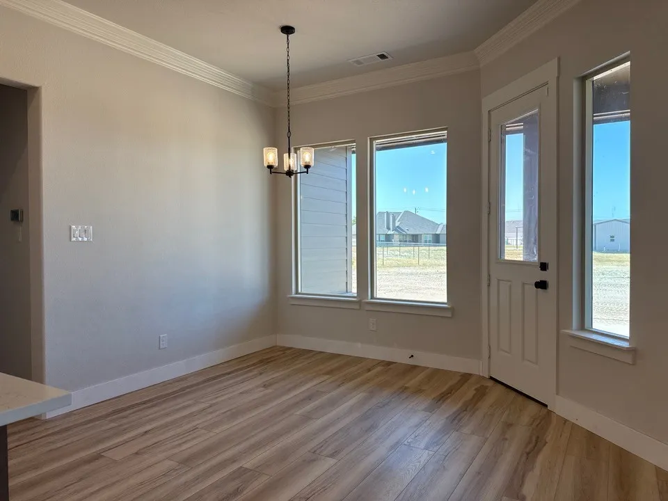 Wood-finish flooring, crown molding, modern chandelier, multiple windows, and a glass-paneled door