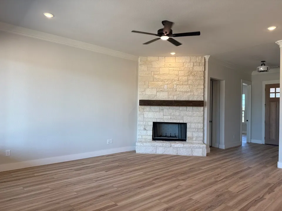 Wood-finish flooring, recessed lighting, and a stone-clad fireplace with a wood mantle and black firebox