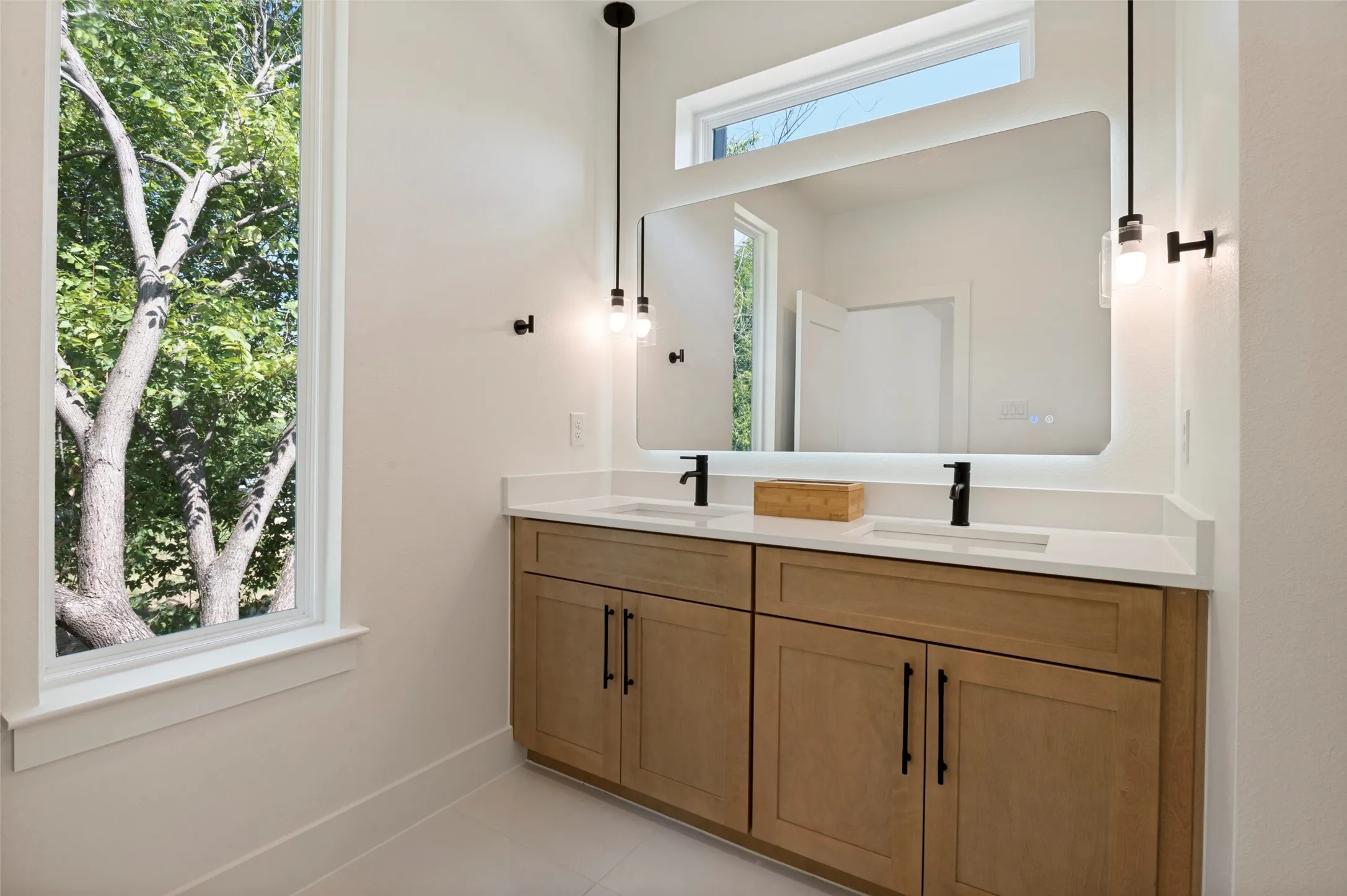 Dual vanity with a light wood-finish cabinetry, white countertop, and matte black fixtures