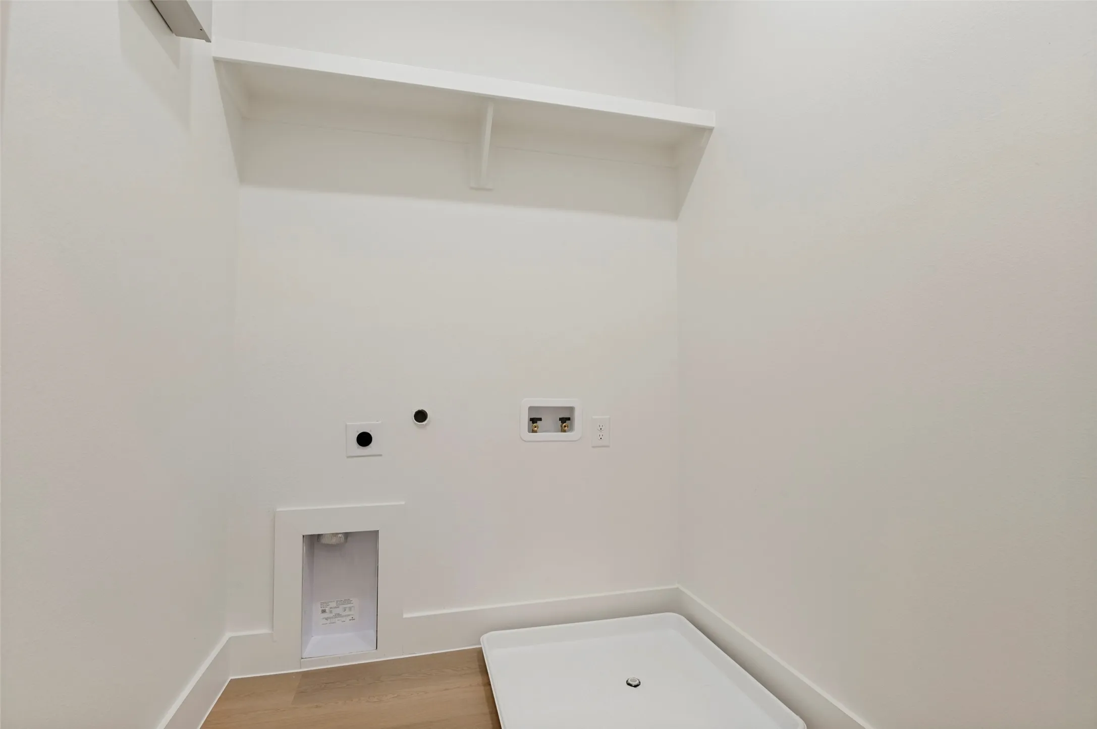 Dedicated laundry area featuring a light wood-finish floor, white walls, and a built-in shelf