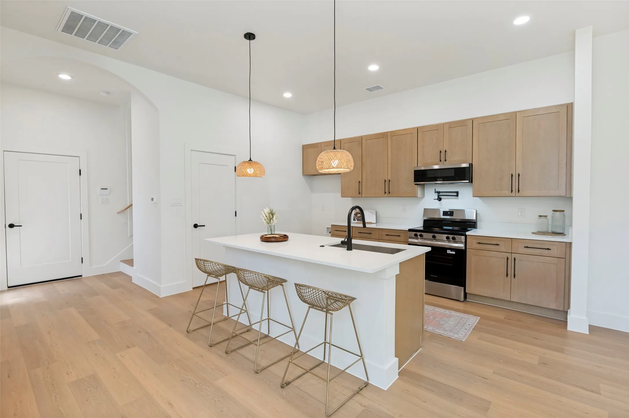 Modern kitchen featuring light wood-finish cabinetry, white countertops, and stainless steel appliances