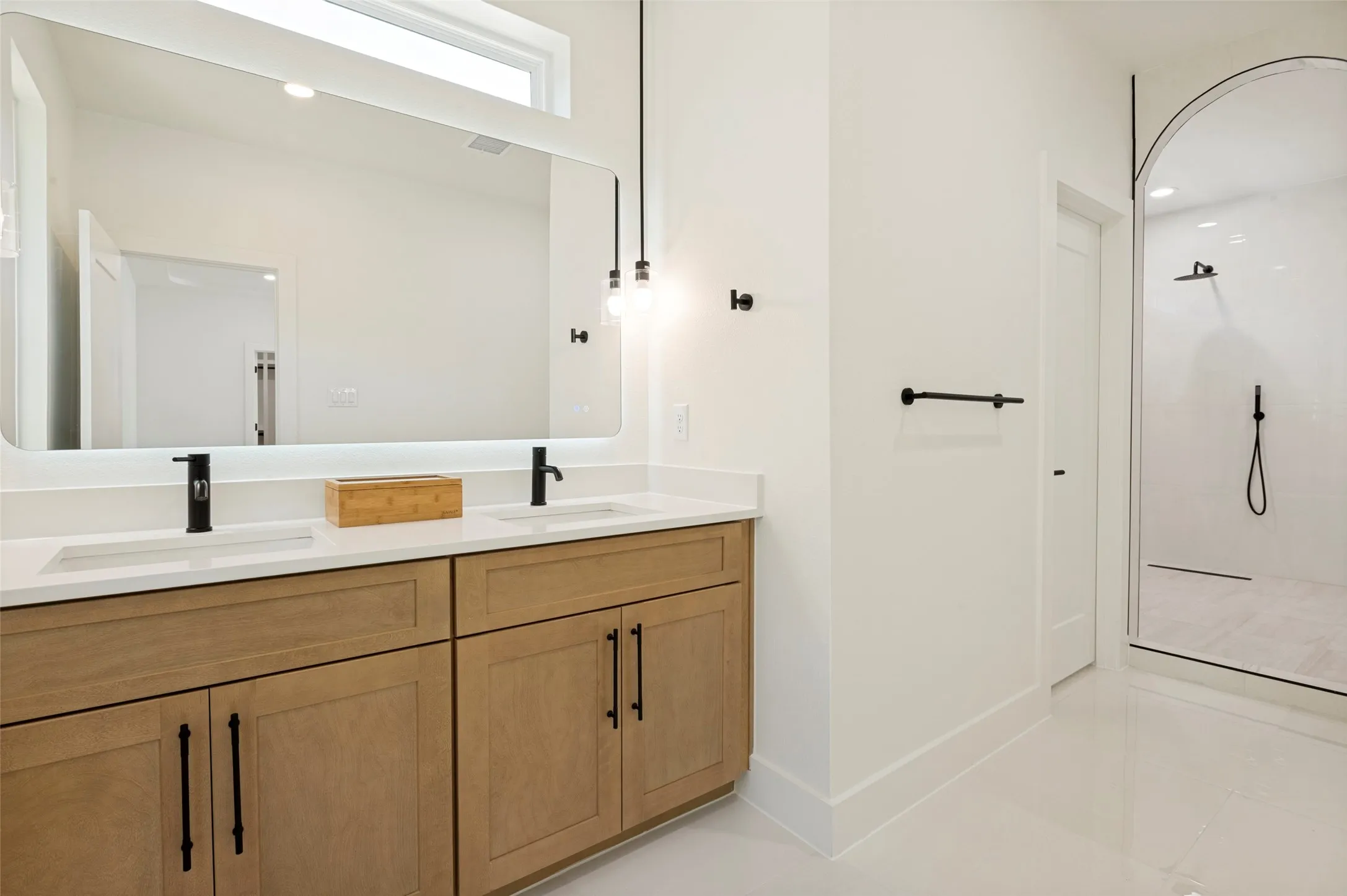 Dual vanity with light wood-finish cabinetry, white countertops, and matte black fixtures