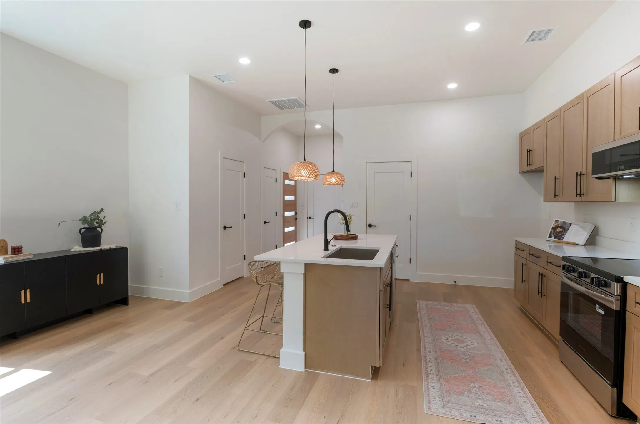 Open-concept kitchen featuring an island with a built-in sink, pendant lighting, light wood-finish flooring, recessed lighting, and stainless steel appliances