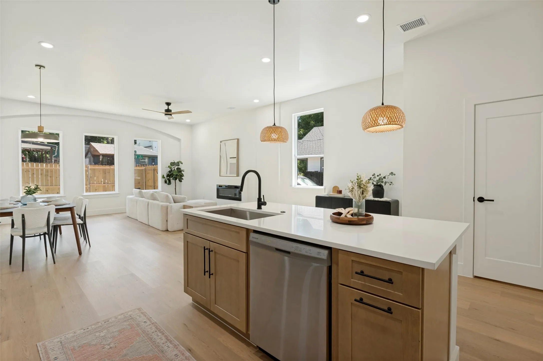 Kitchen island featuring an undermount stainless steel sink, black gooseneck faucet, light wood-finish cabinetry with black hardware, and an integrated dishwasher