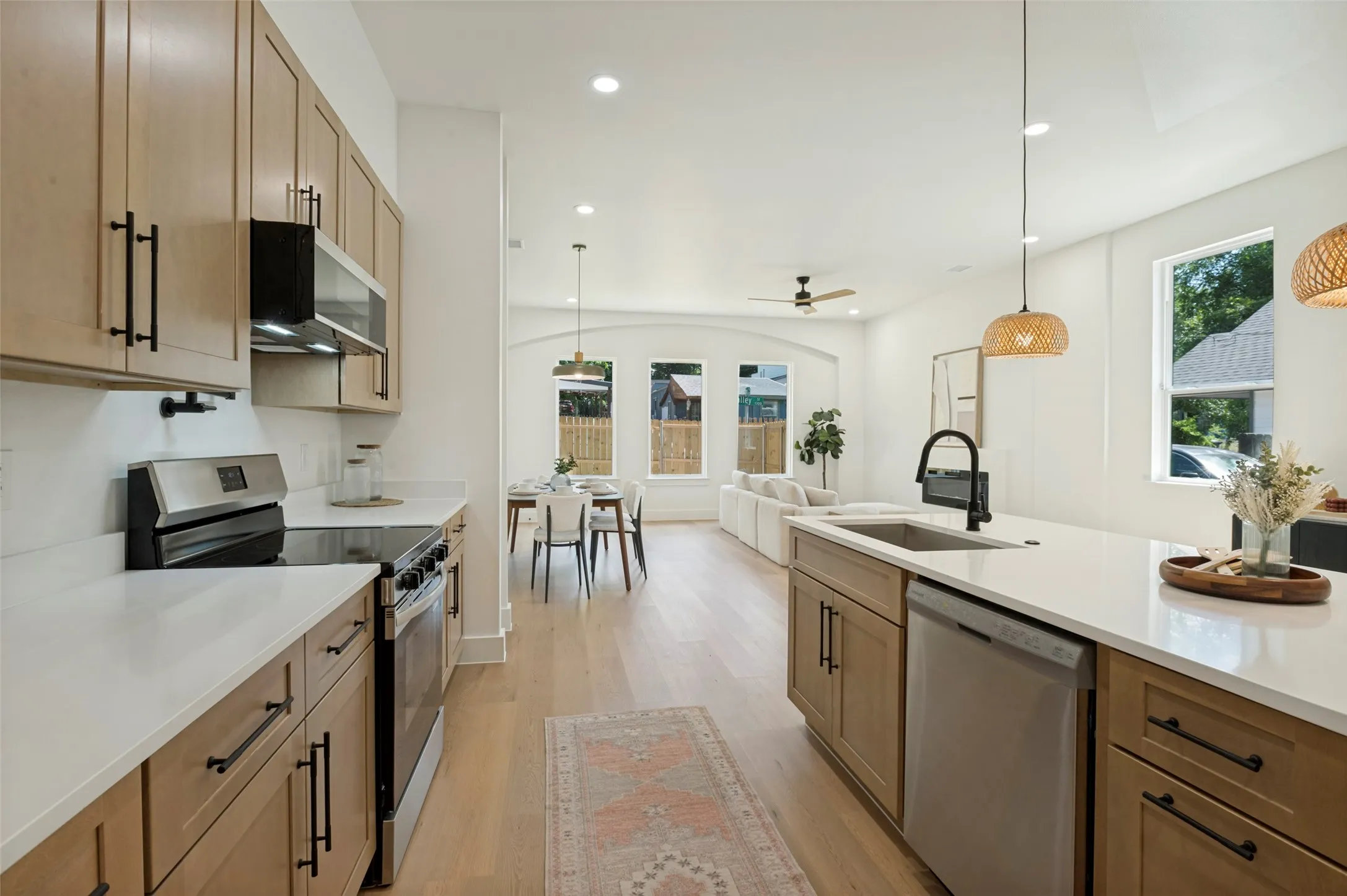 Open-concept kitchen featuring light wood-finish cabinetry, stainless steel appliances, white countertops, and light wood-finish flooring