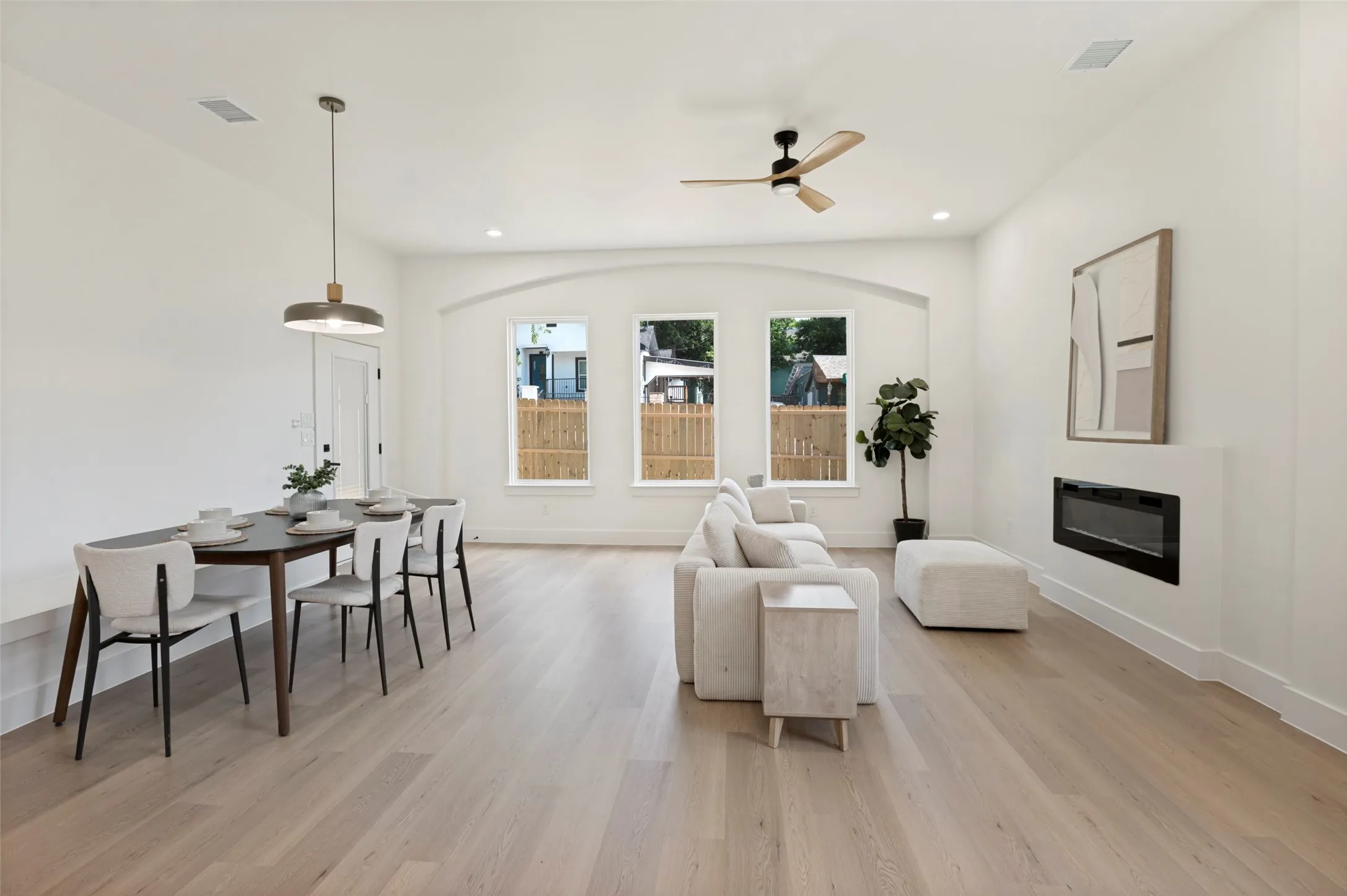 Open-concept interior featuring wood-finish flooring, a wall-mounted electric fireplace, and an arched window alcove with three large windows