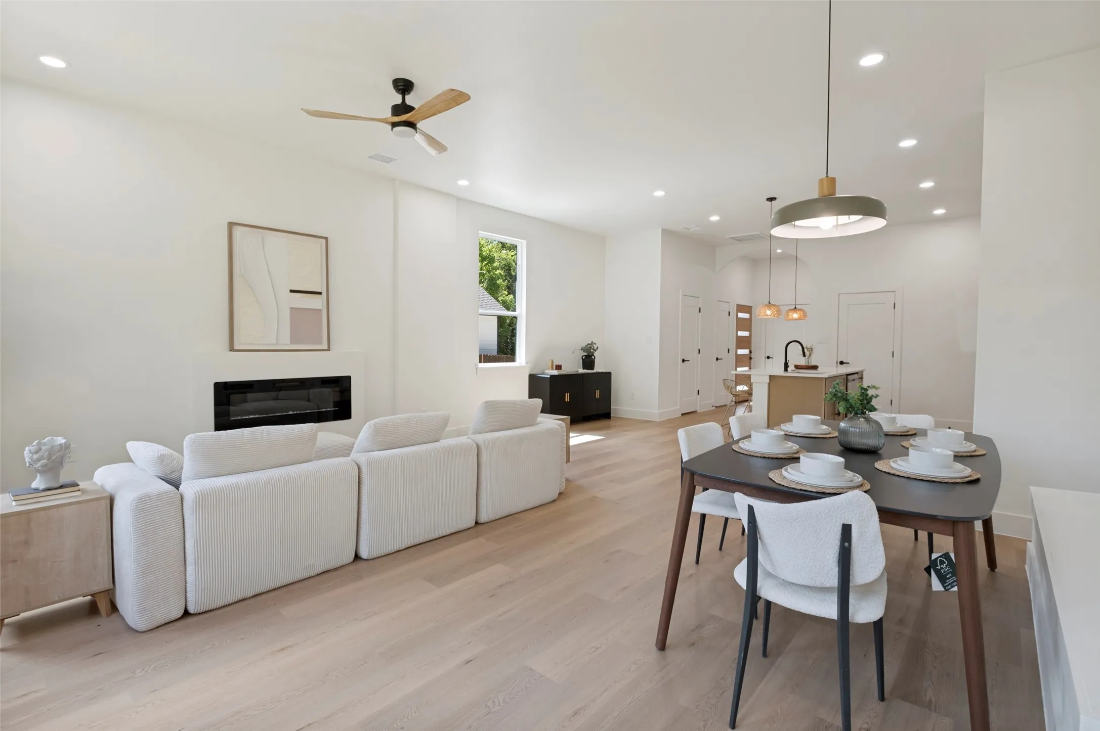 Open-concept living space featuring light wood-finish flooring, recessed lighting, and a modern fireplace with a white surround