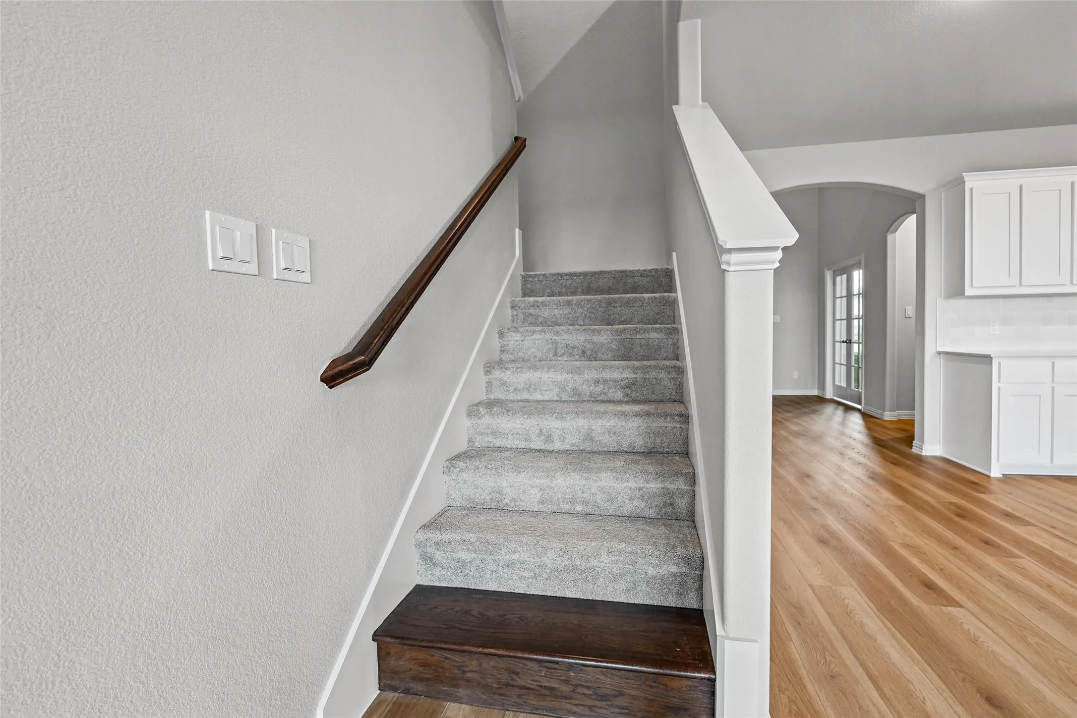 Carpeted staircase with a wood-finish handrail, wood-finish flooring, and white cabinetry