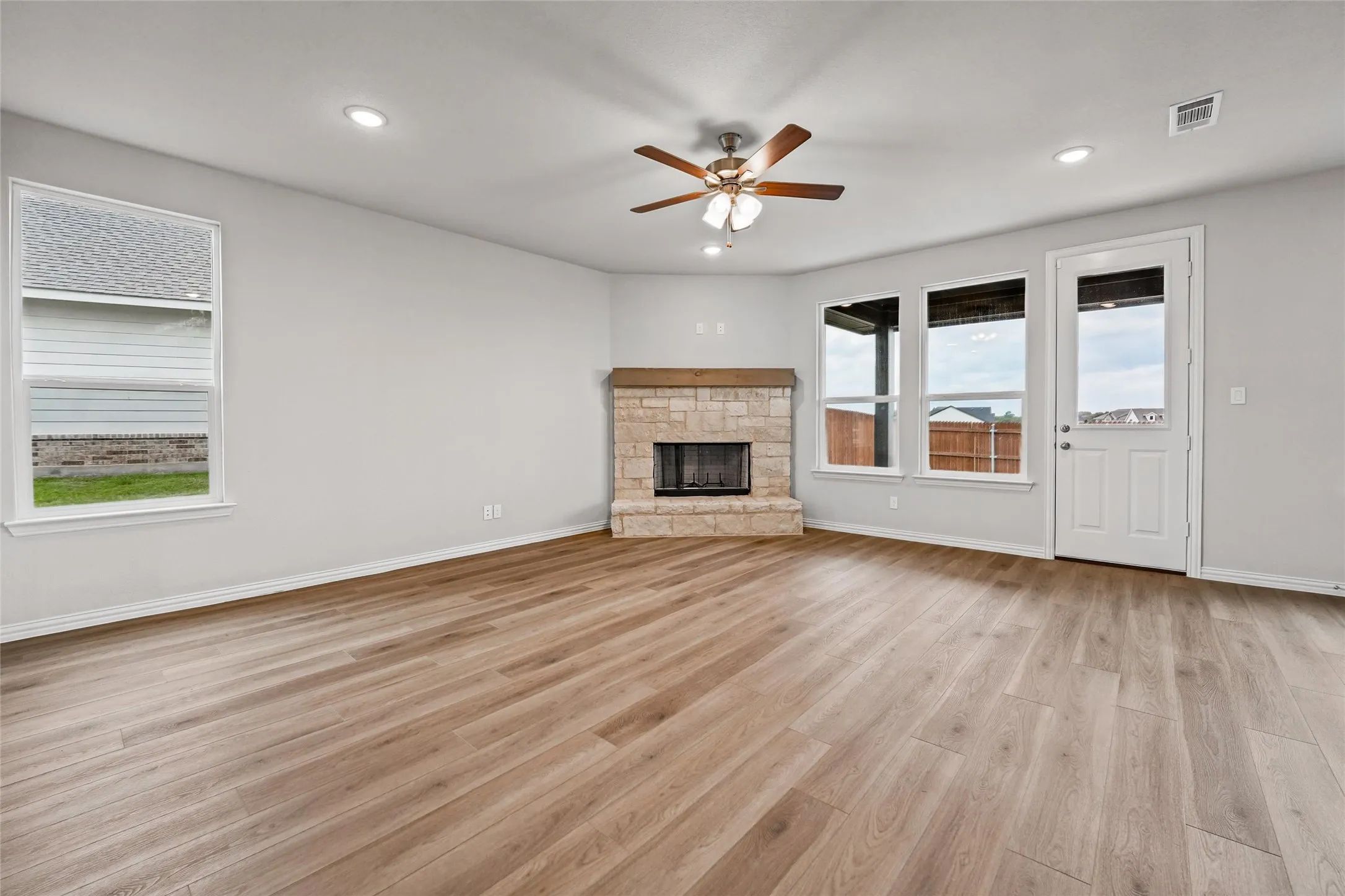 Wood-finish flooring, recessed lighting, and a stone-faced fireplace with a wood mantle