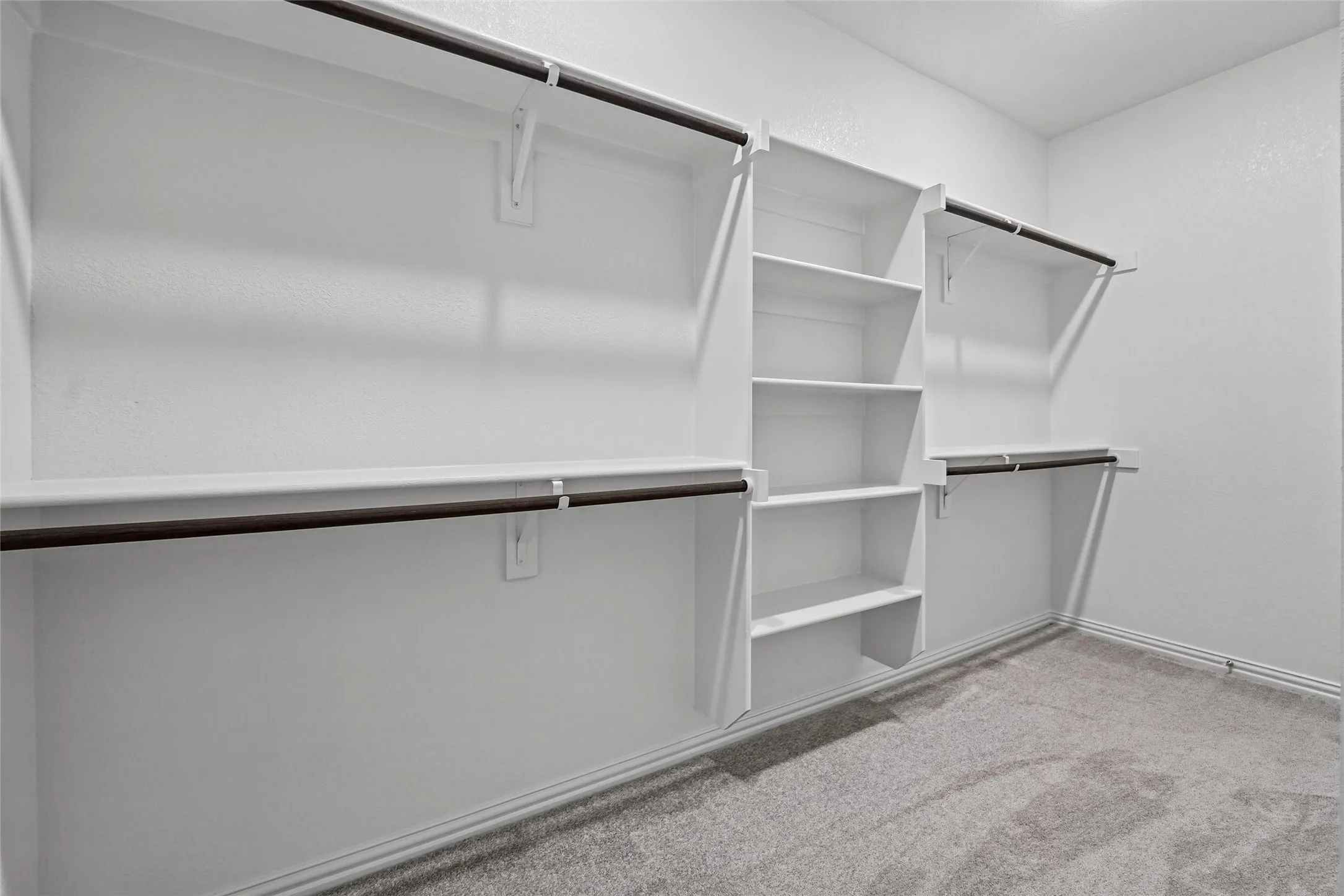 Built-in shelving, multiple hanging rods, and light gray carpeting