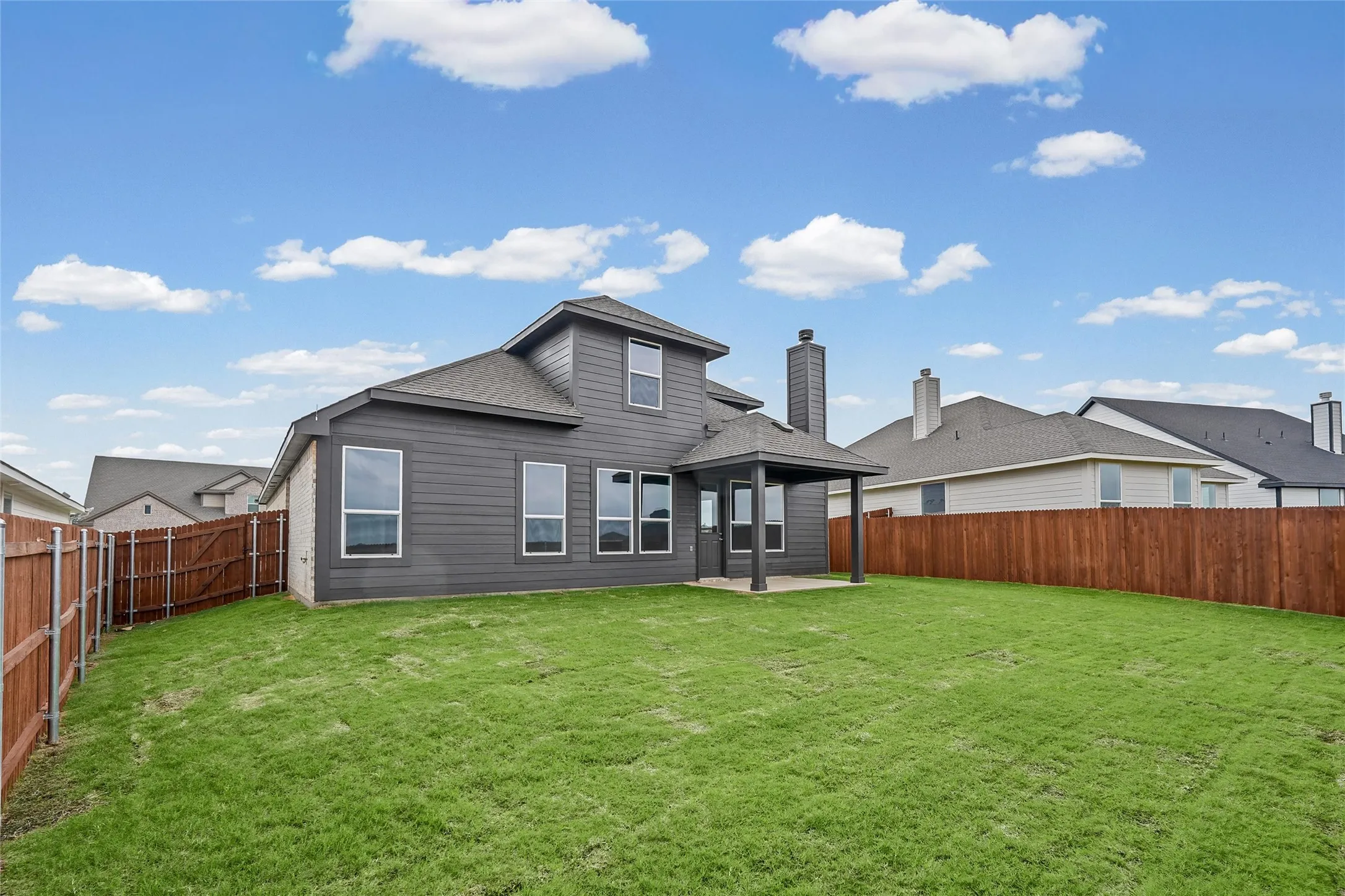 Expansive backyard featuring a covered patio, dark siding, multiple windows, and a wood privacy fence