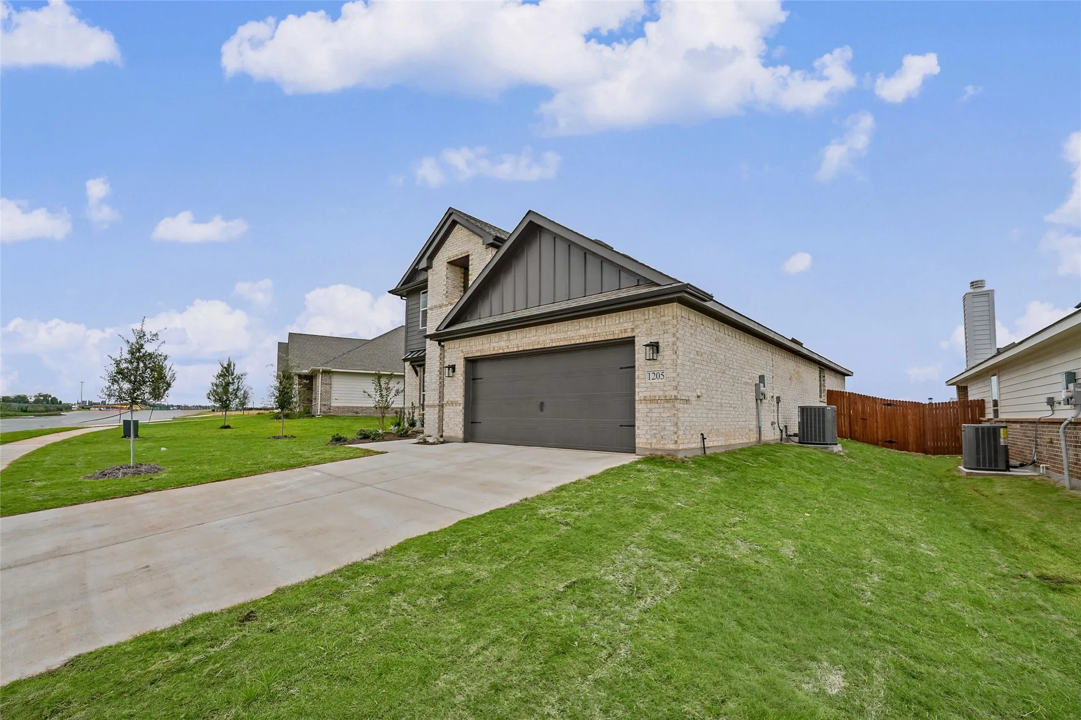 Brick exterior featuring a two-car garage with a dark gray door, concrete driveway, and established landscaping
