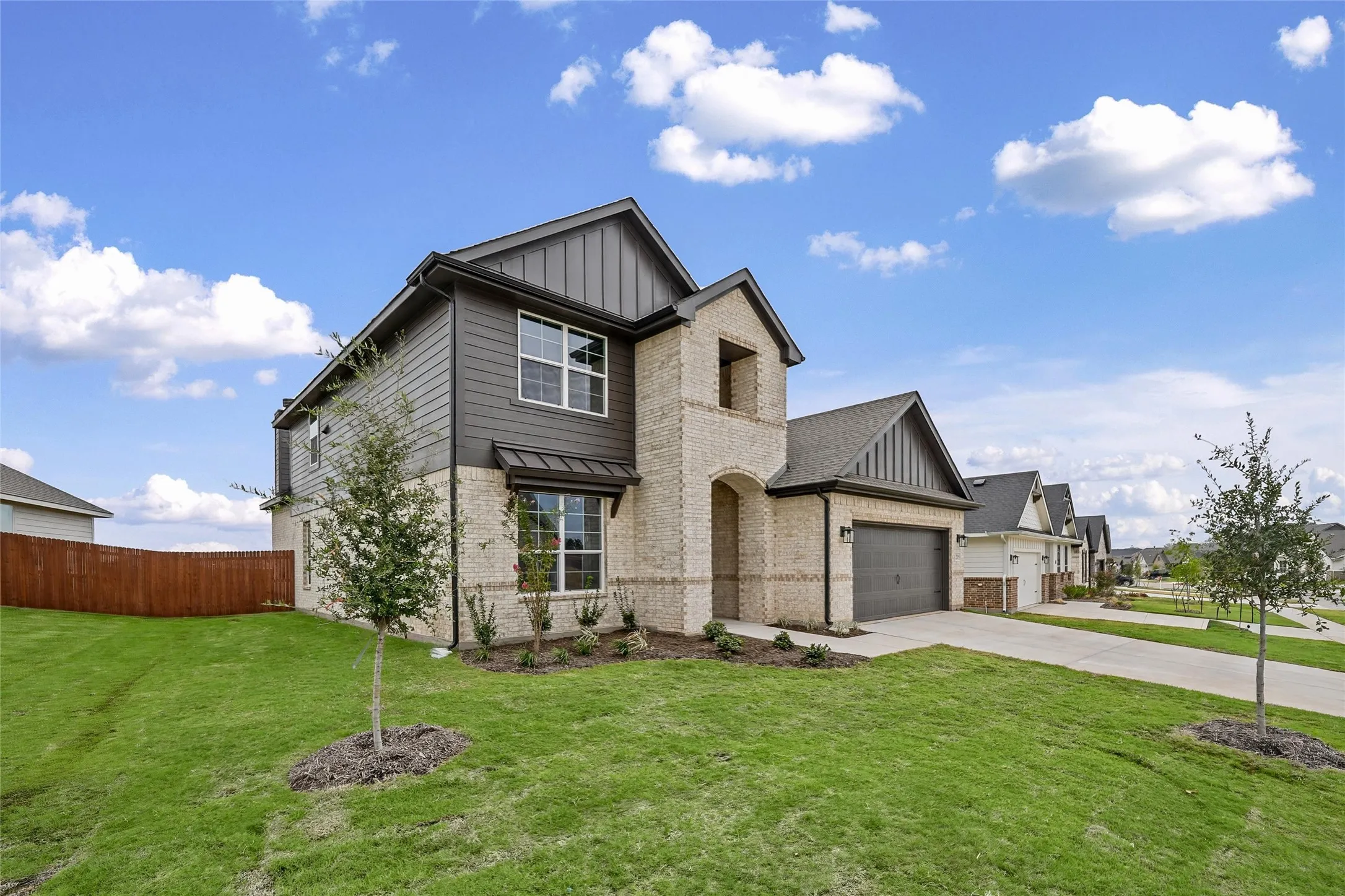 Two-story exterior featuring a brick and siding facade, covered front entry, attached garage, and a manicured lawn